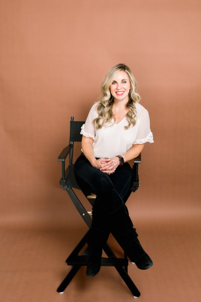 Scottsdale Social Media Manger wearing a a white blouse and black pants sitting on a black director's chair on a terricata backgroud at Studio House AZ in Phoenix Arizona by Danielle Muccillo Photography
