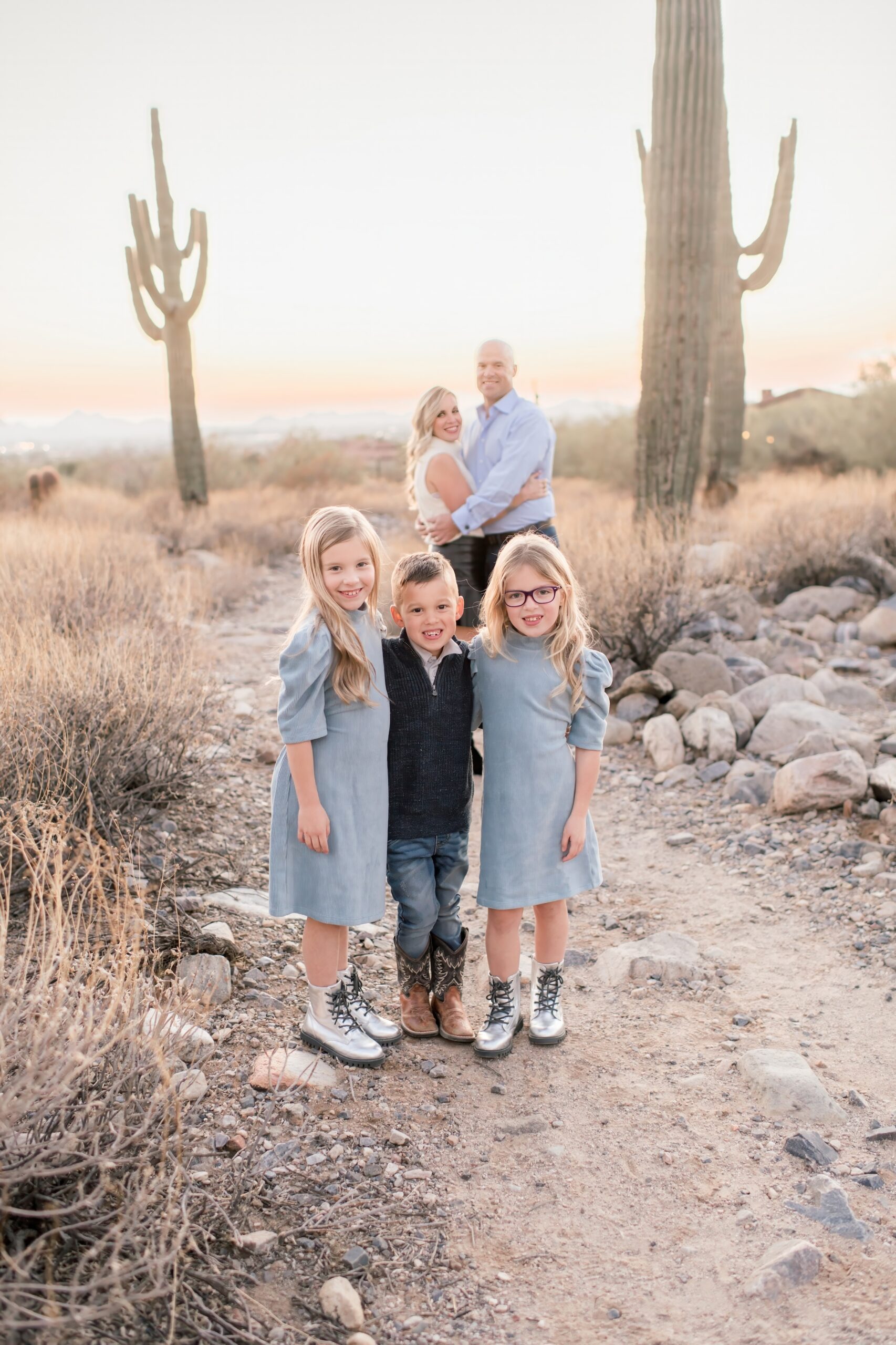 Family of 5 Mom and Dad behind the 3 kids standing in the arizona desert at sunset.