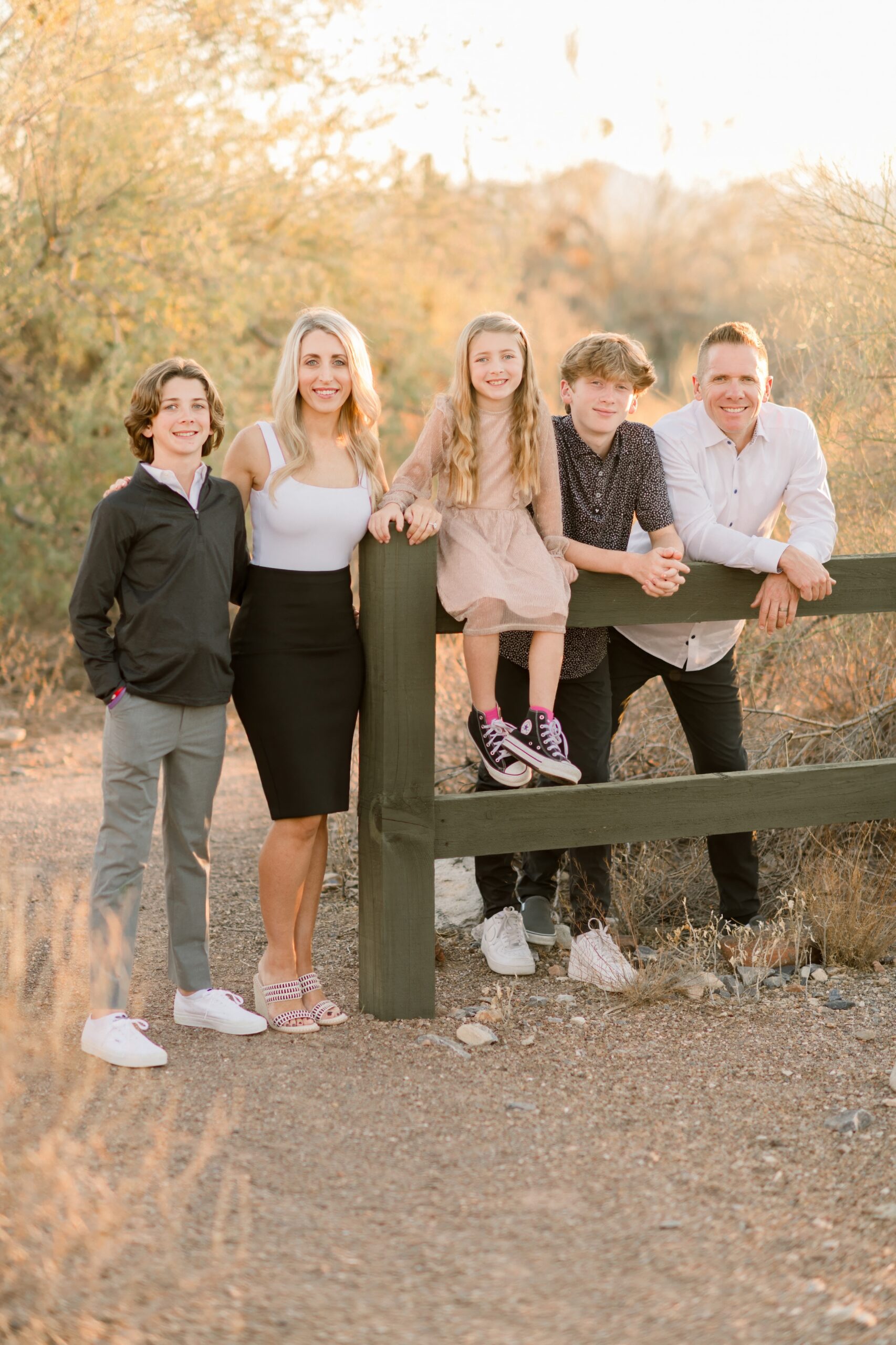 Mom, dad, two boys leaning on a fence while their sister is sitting on it.