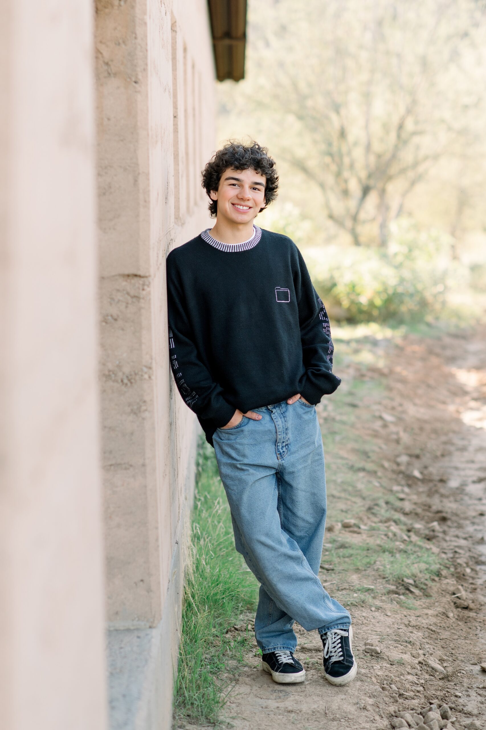 Senior boy wearing a black sweater top and jeans leaning against a wall the desert