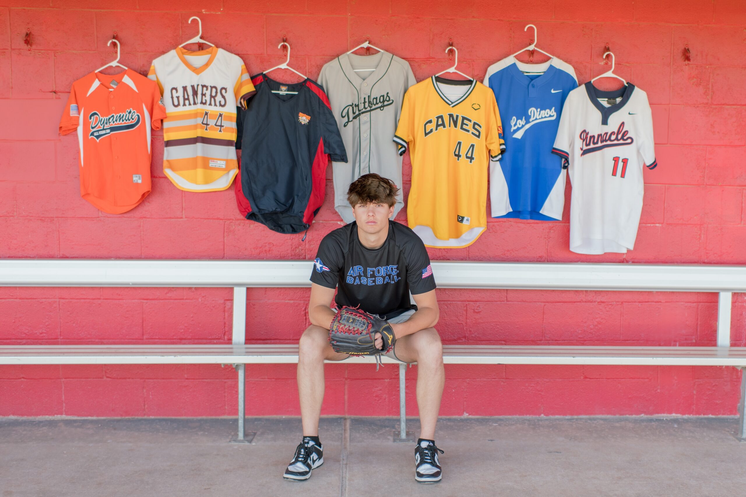 Senior boy wearing an air force academy shirt, sitting on a bench with 7 youth jesery's behind him.