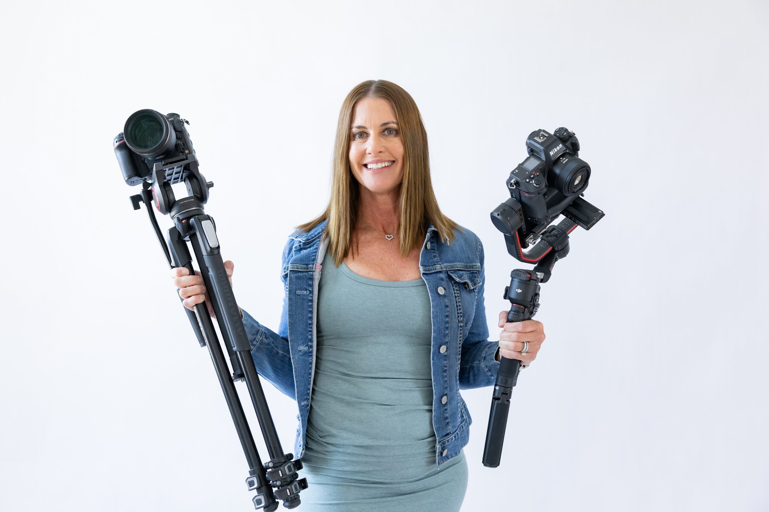 Owner Danielle Muccillo of Danielle Muccillo Photography, holding two camera one on a gimble and one on a tripod smiling at the camera in Scottsdale Arizona