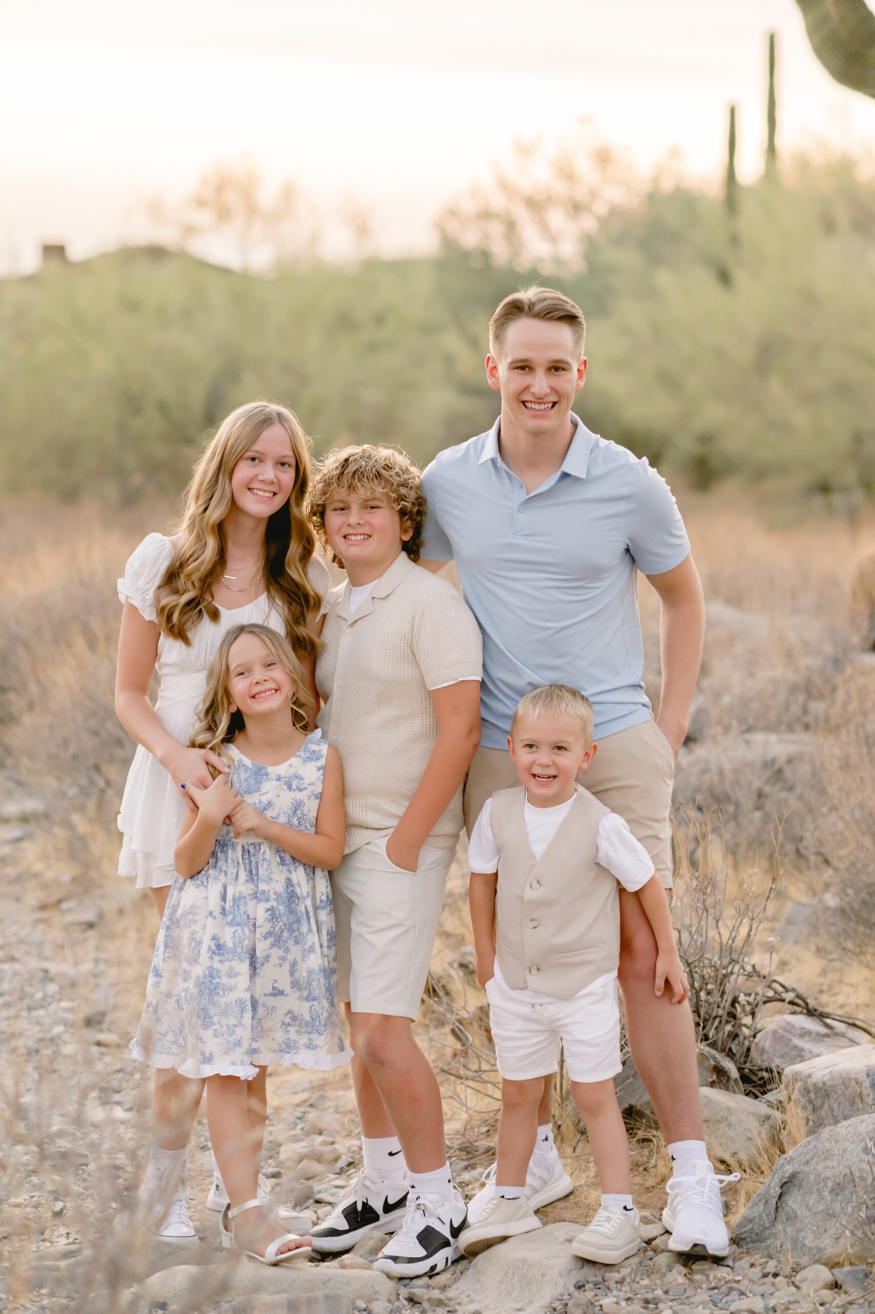 family of 5 kids standing and smiling at the camera in the arizona desert all wearing neutral colored tops and dresses.