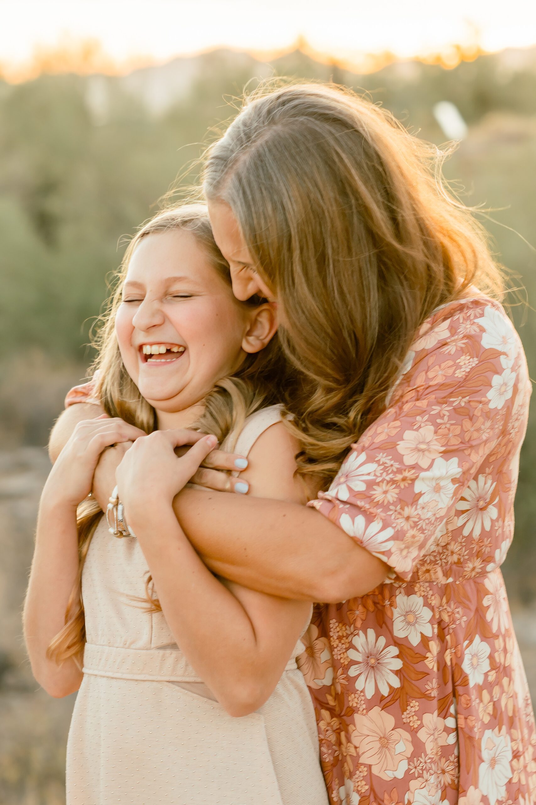 mom hugging daughter in phoenix arizona desert daughter has on a tan dress and mother has on a floral orange dress