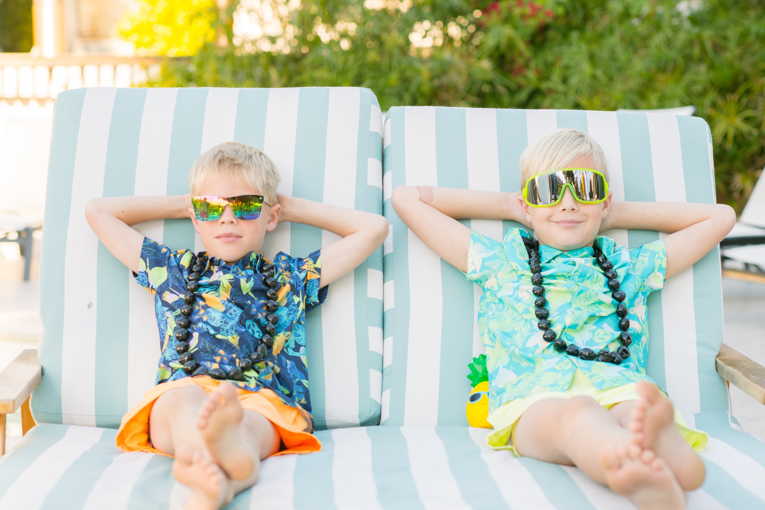 Toddler brothers lounge on patio couch in tropical shirts and big sunglasses at family friendly hotels in phoenix