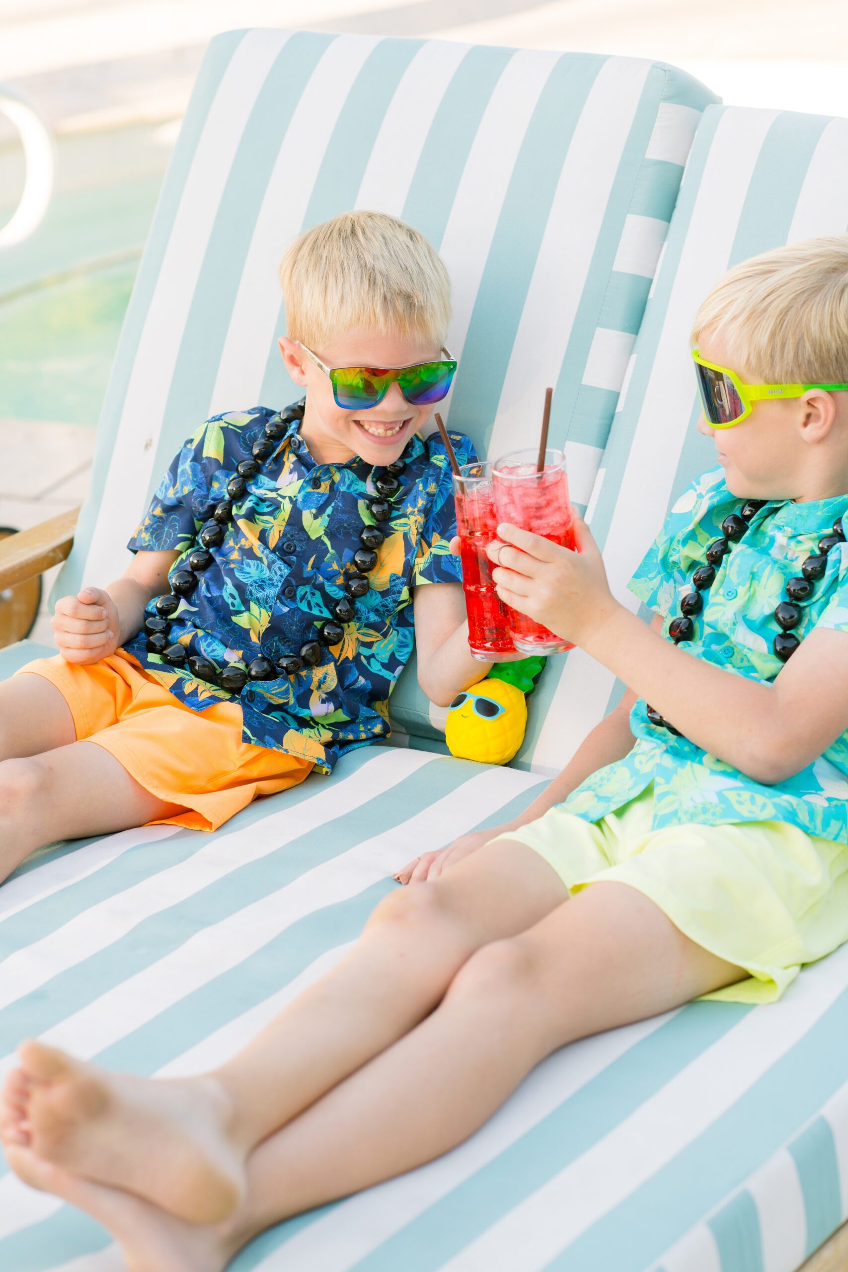Two brothers in Hawaiian shirts toast their red drinks in a lounger couch at one of the family friendly hotels in phoenix