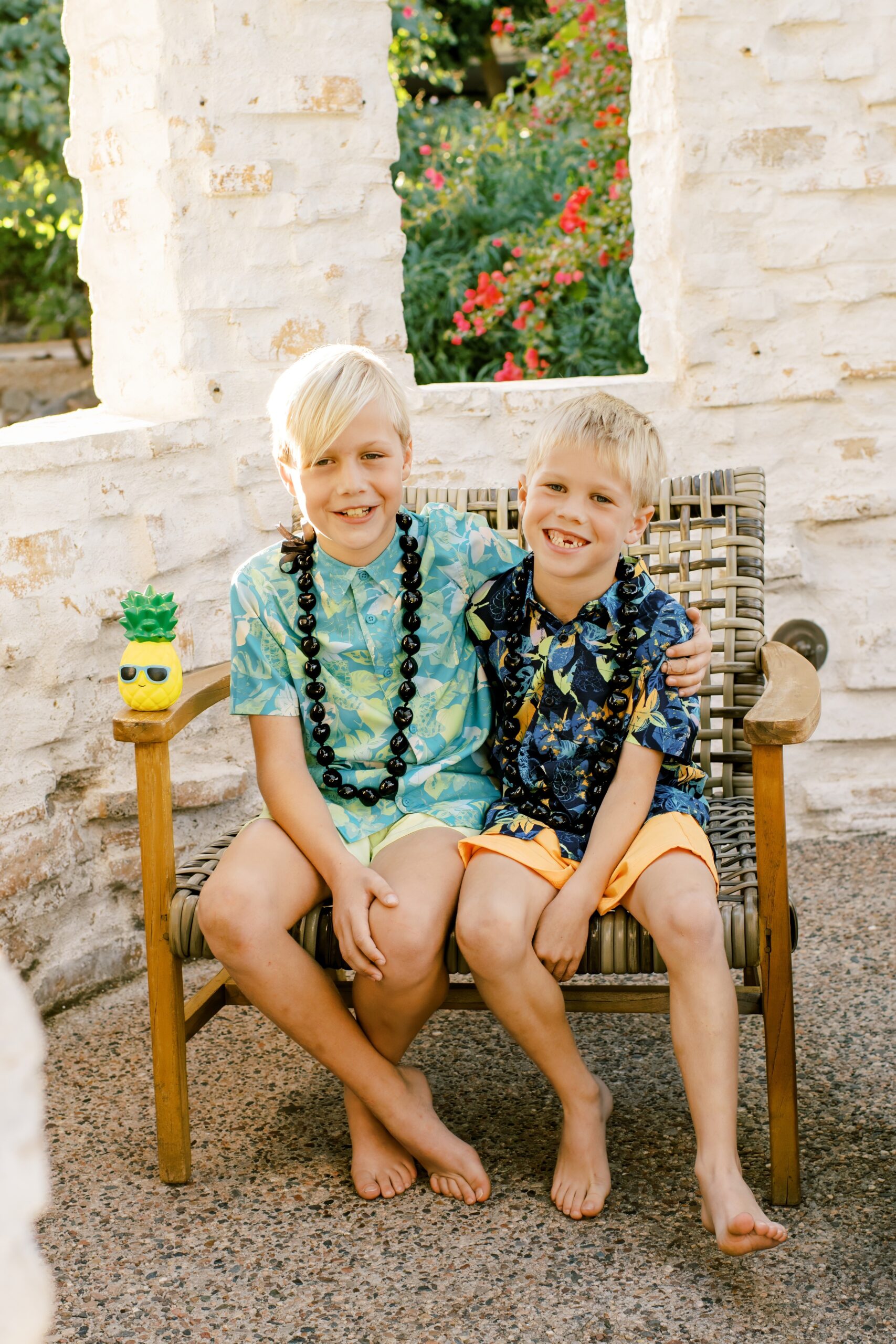 Young brothers sit on a wicker chair in a garden smiling in floral tropical shirts at family friendly hotels in phoenix