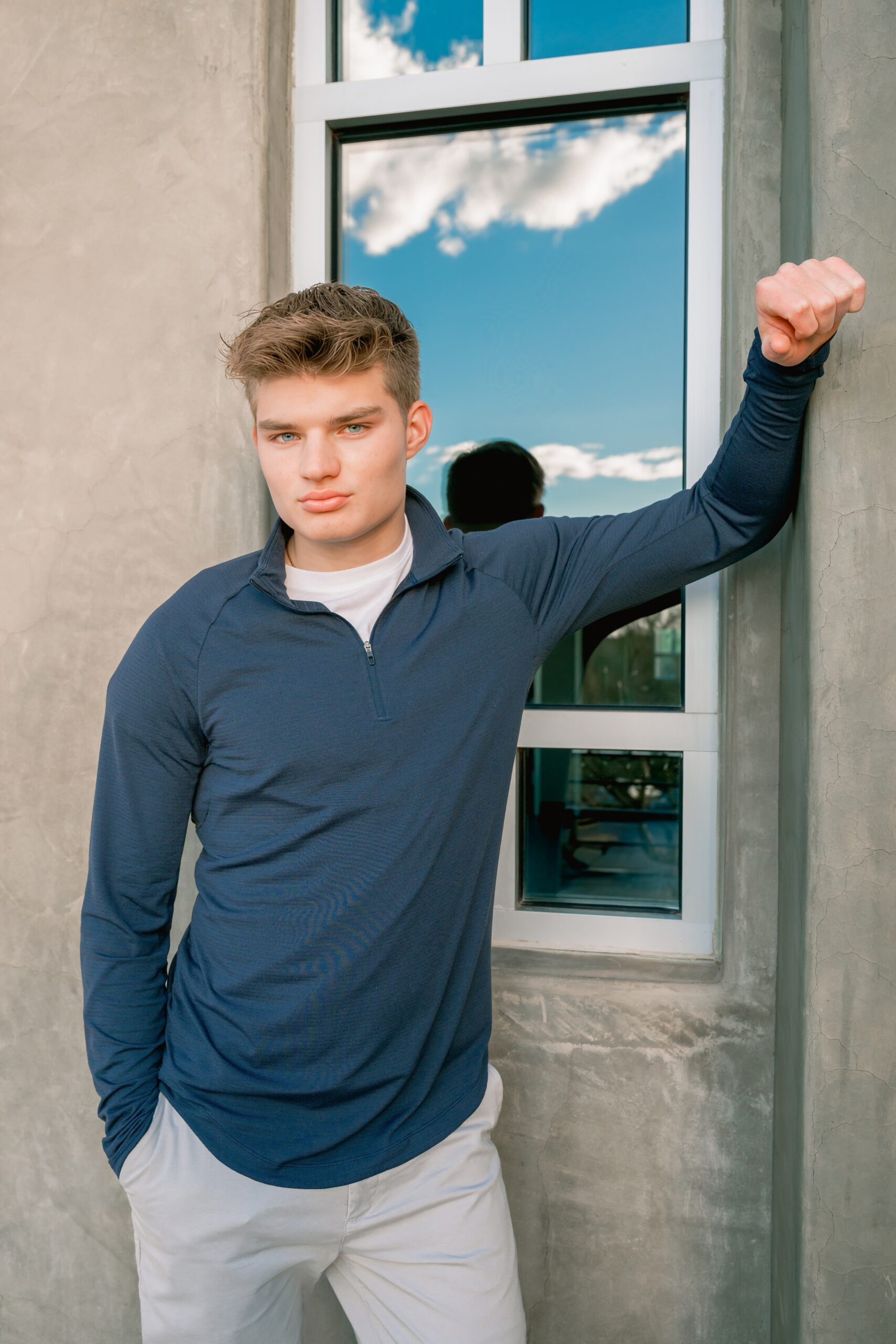 A pinnacle high school senior in a blue sweater leans in a window outside with a model face