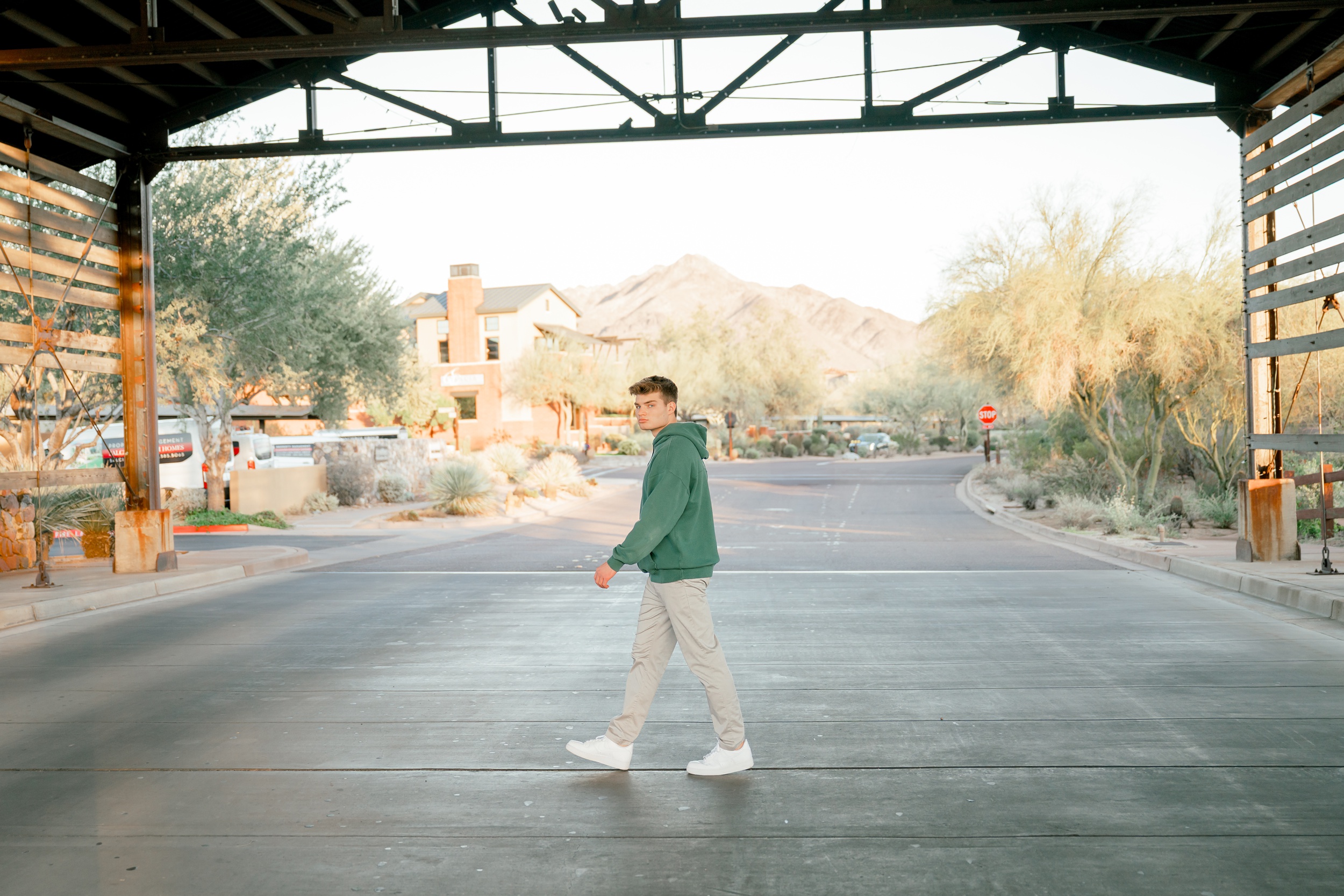 A pinnacle high school in a green hoodie and tan pants walks under a rustic covering looking over his shoulder