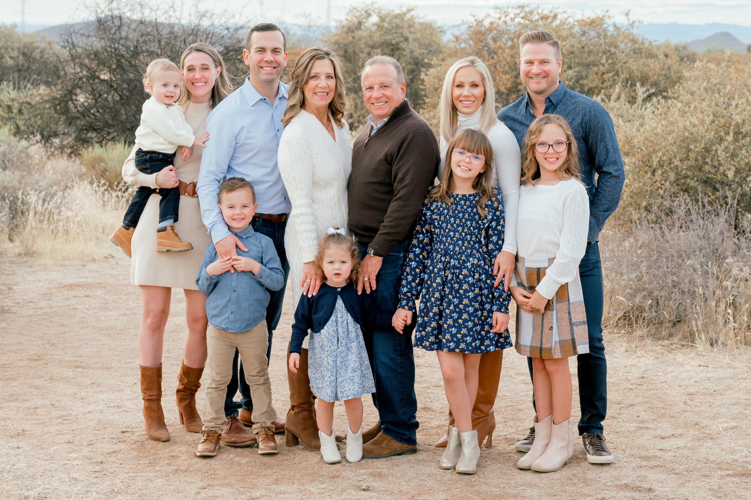 An extended family with four little ones smiles in a desert trail with mountains in background