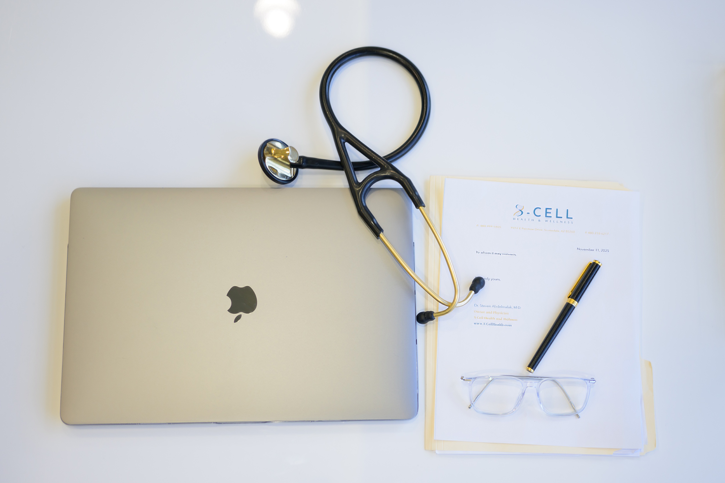 A laptop lays on a table with a file and stethoscope