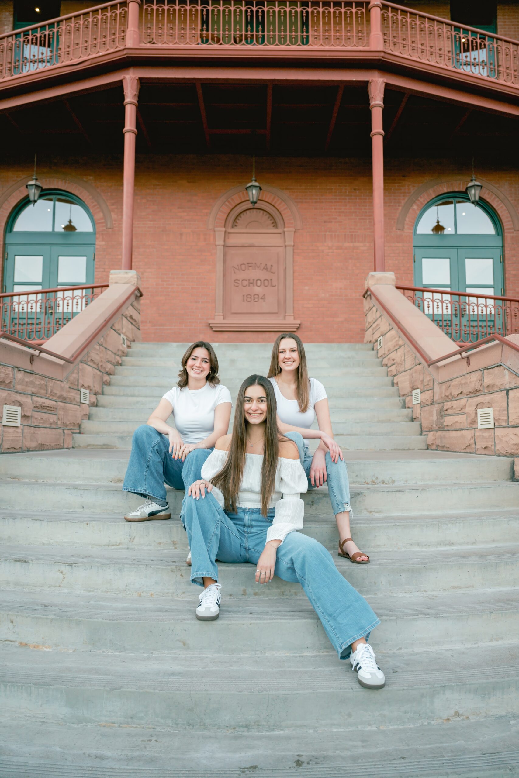 Three graduates sit on concrete stairs of an old building after visiting colleges in arizona