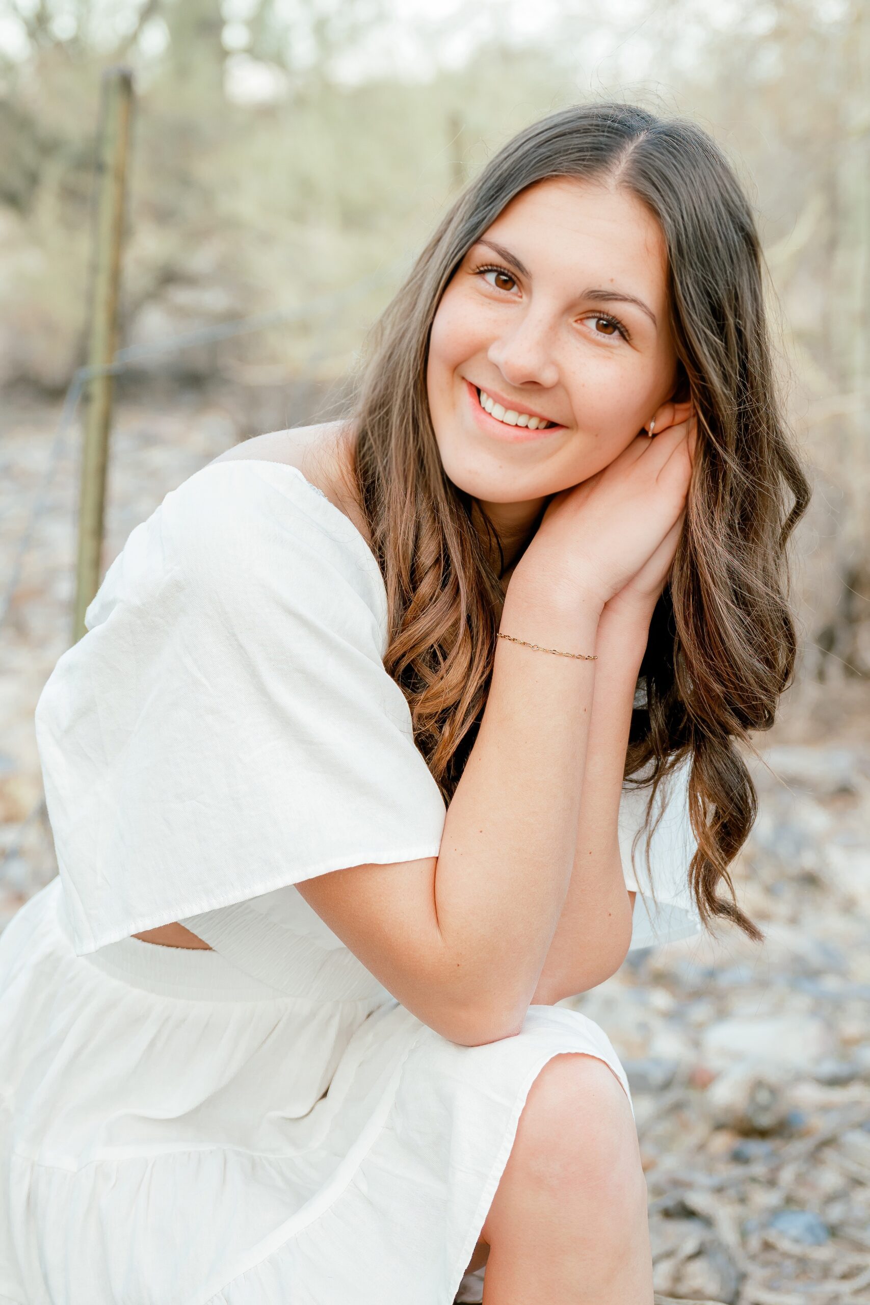 A happy teen in a white dress leans on her knee smiling in the desert