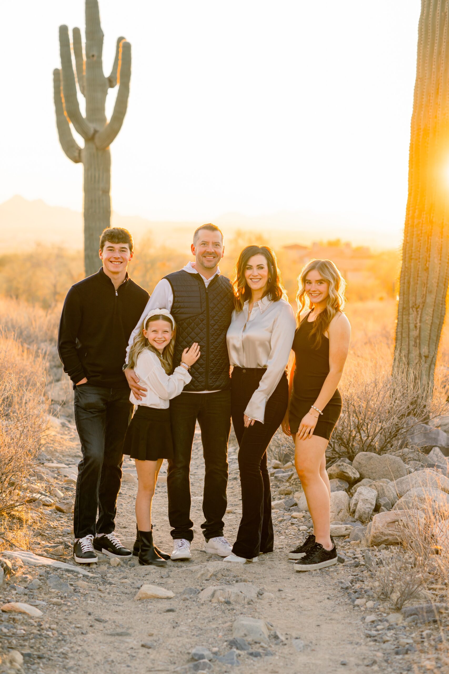 A happy family of 5 hug and smile while hiking in the desert at sunset before visiting indoor playgrounds in scottsdale