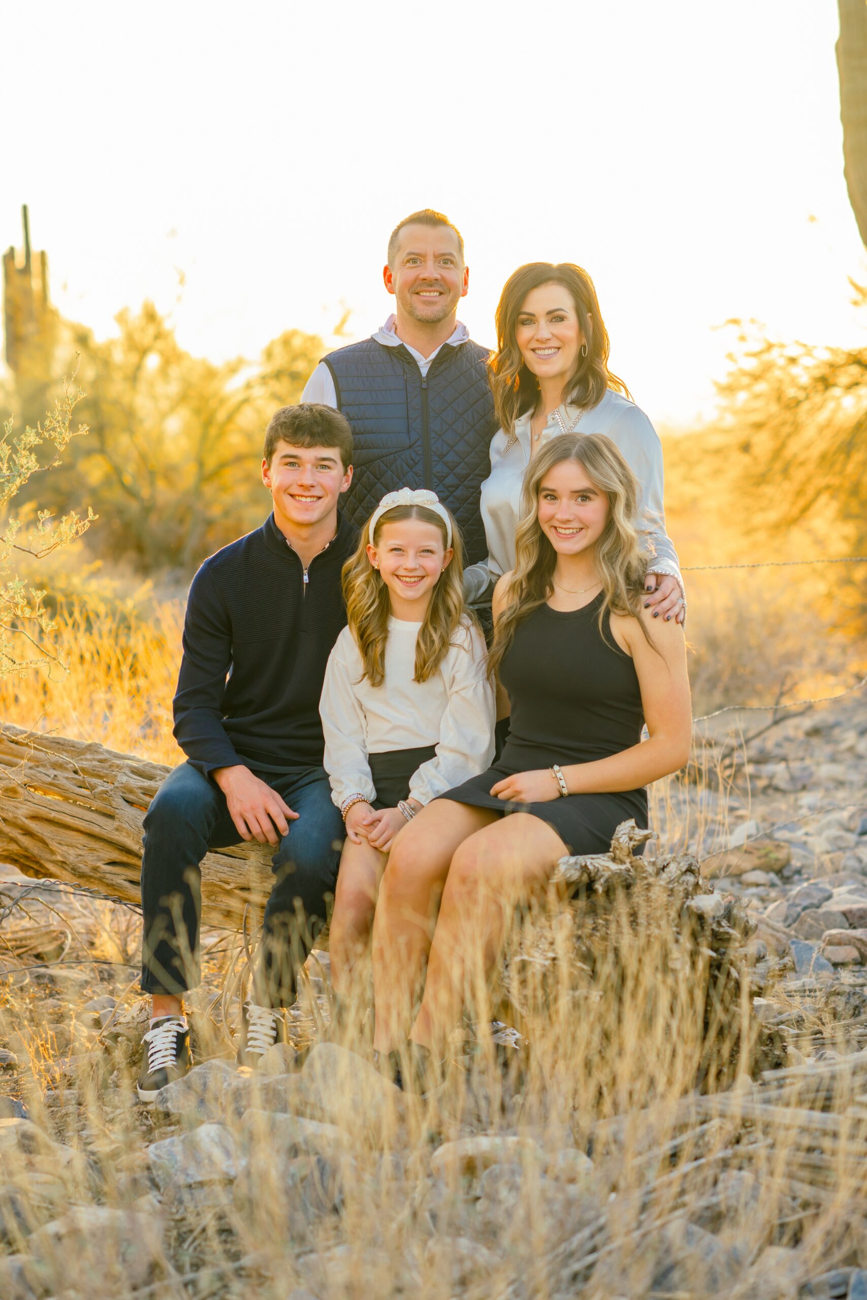 Three siblings sit on a fallen tree with mom and dad standing behind them before visiting indoor playgrounds in scottsdale
