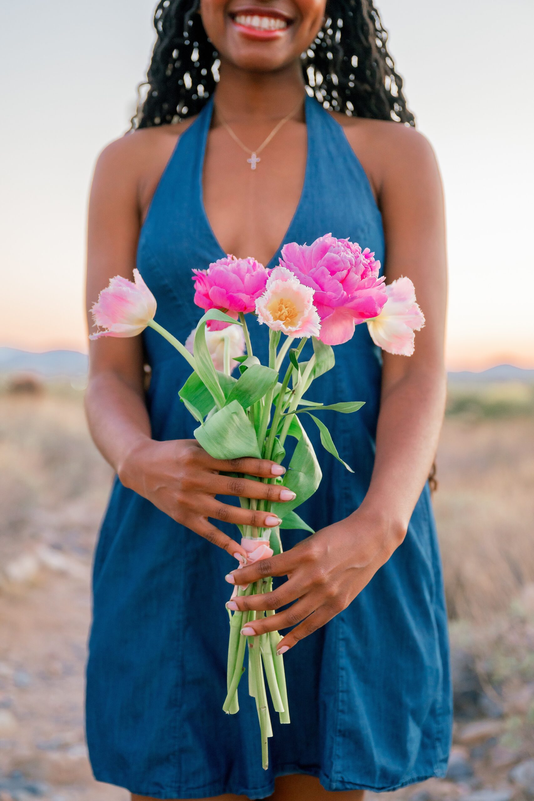 A woman holds pink flowers out in front of her while in a blue dress