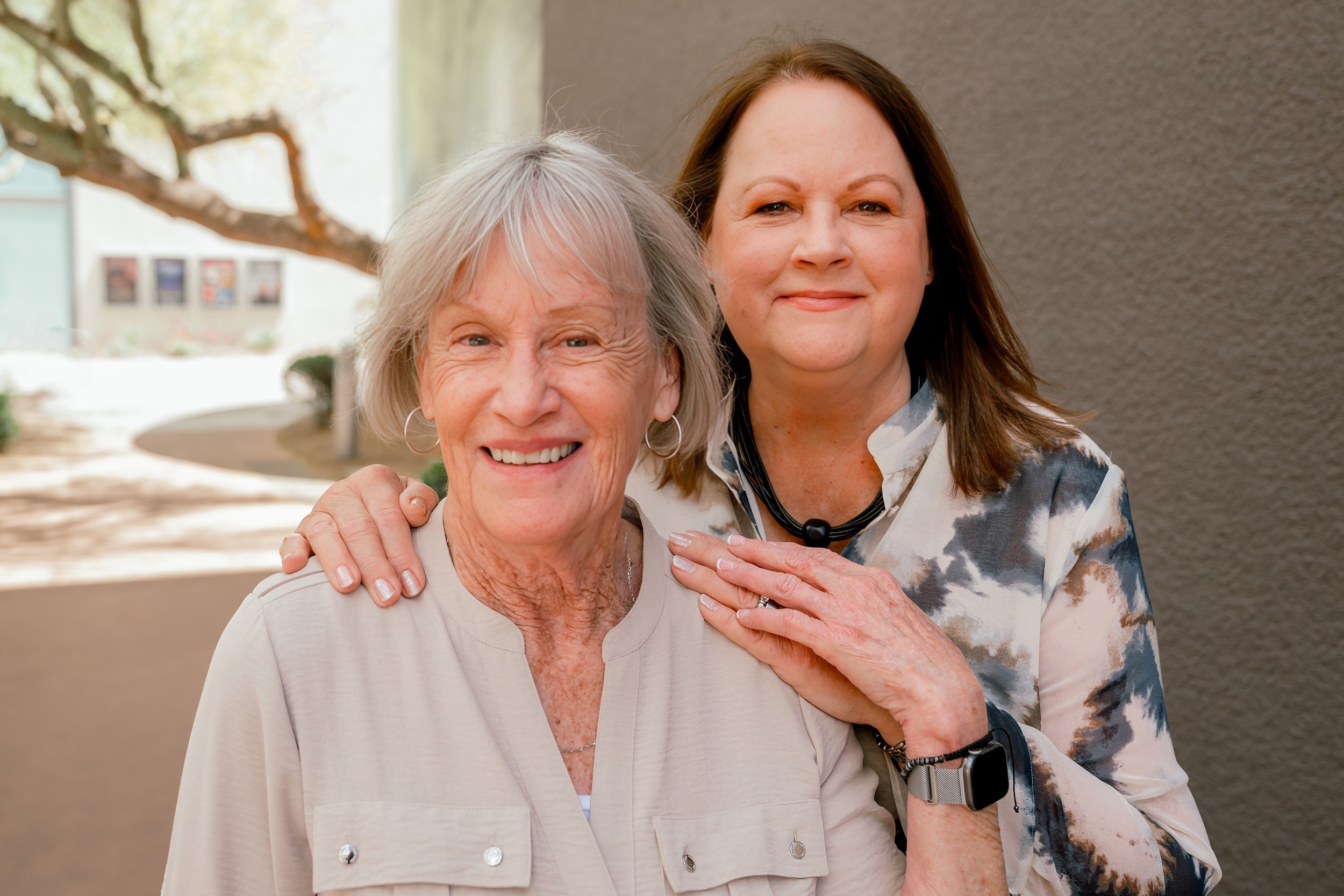 A woman leans on her mother while standing in the shade