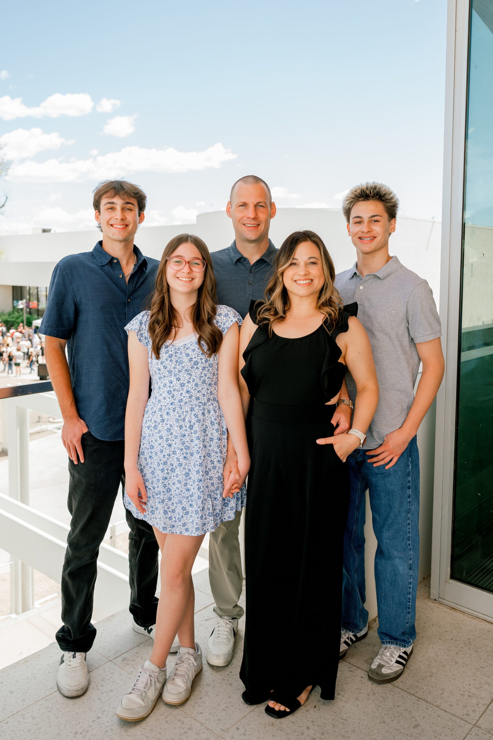 A mom and dad smile big while standing on a balcony with their three teenage children