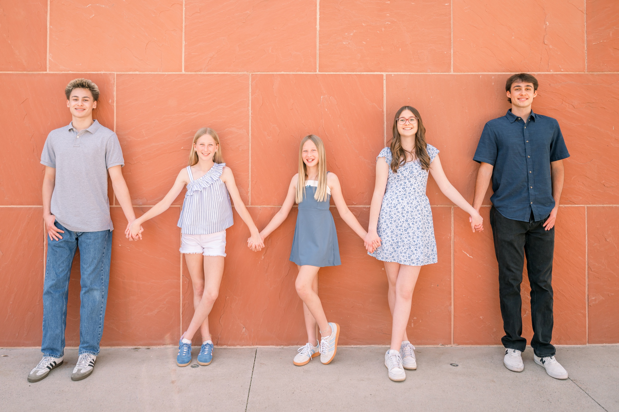 A group of siblings hold hands and smile while leaning on an orange wall at one of the old town scottsdale photo spots