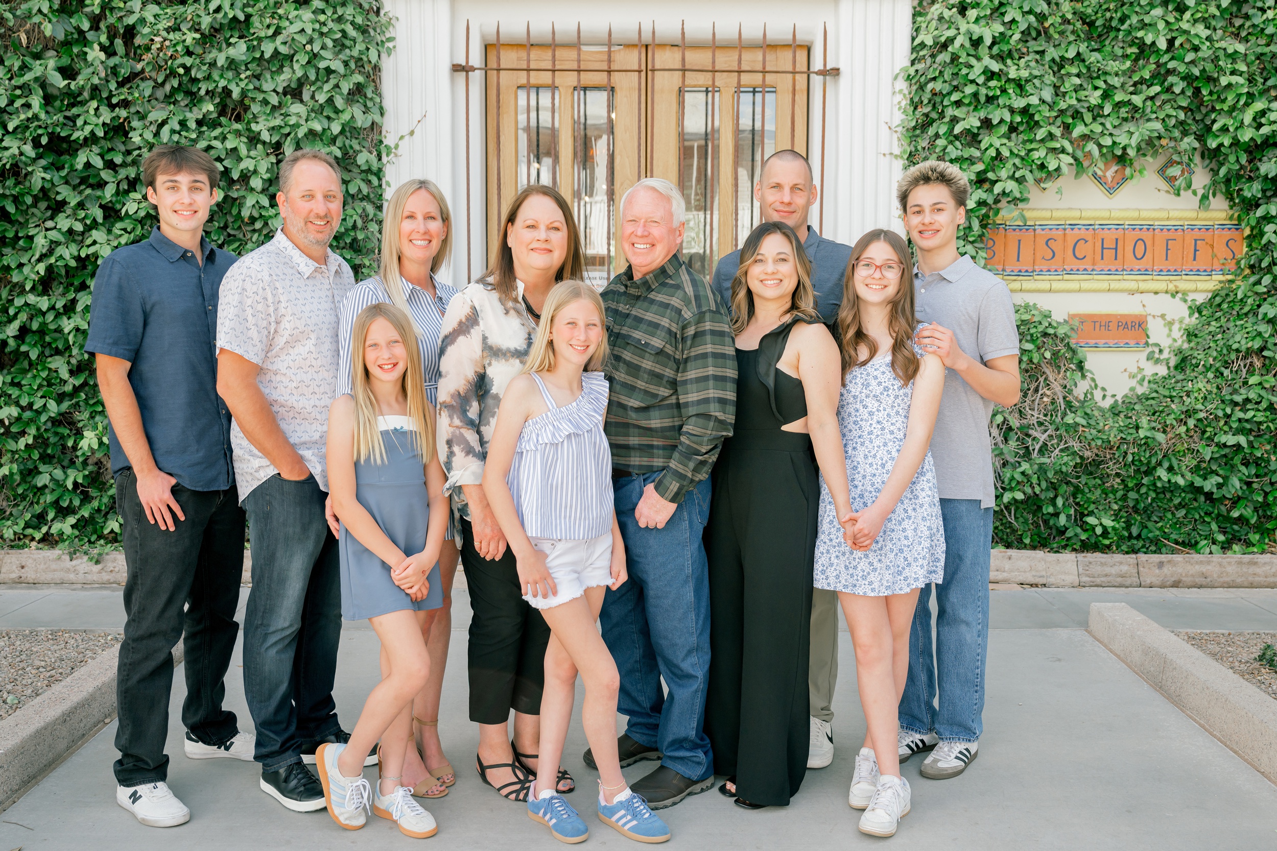 A happy extended family stand smiling together in front of one of the old town scottsdale photo spots with ivy covered walls