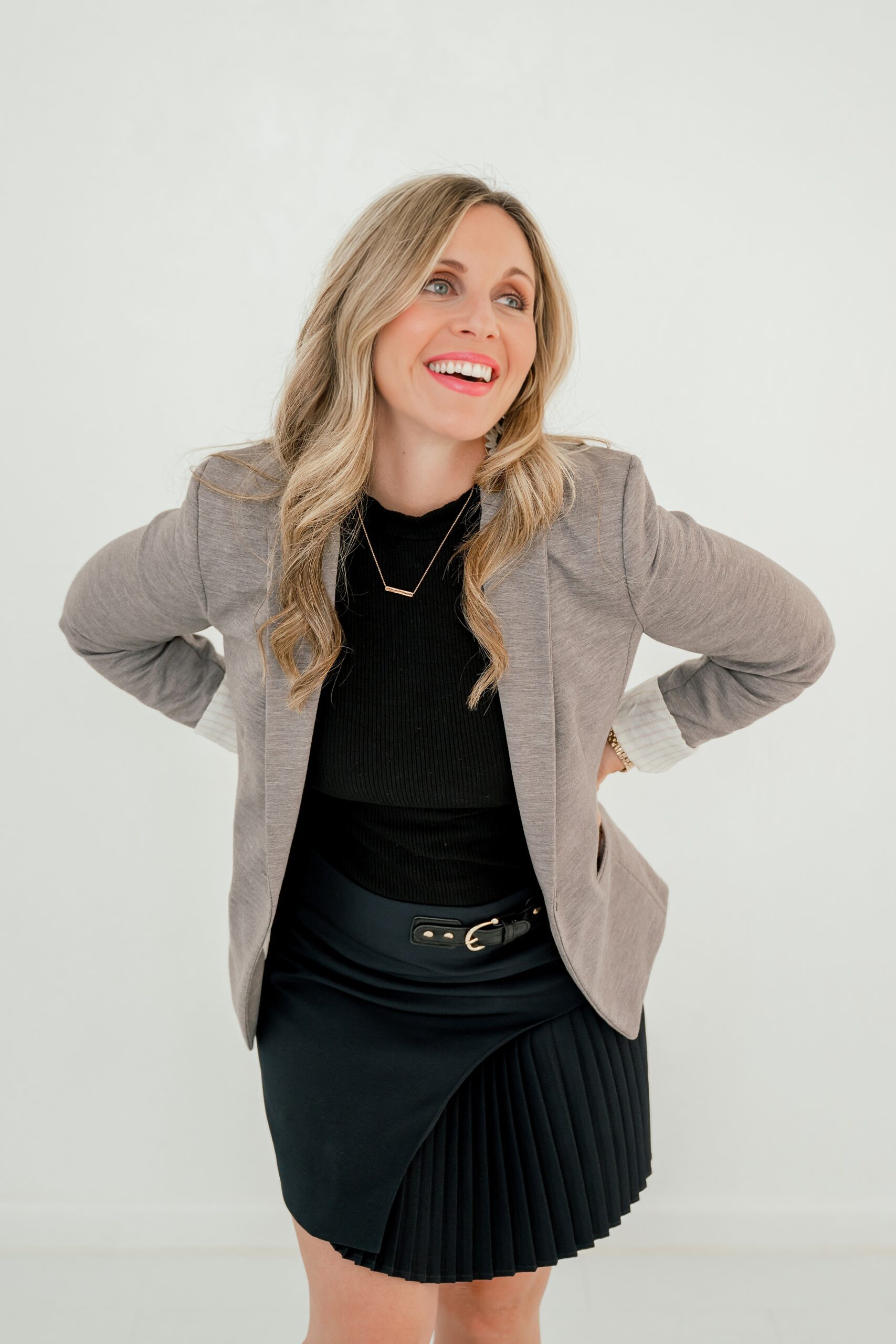 A happy woman laughs over her shoulder while wearing a black dress and tan coat