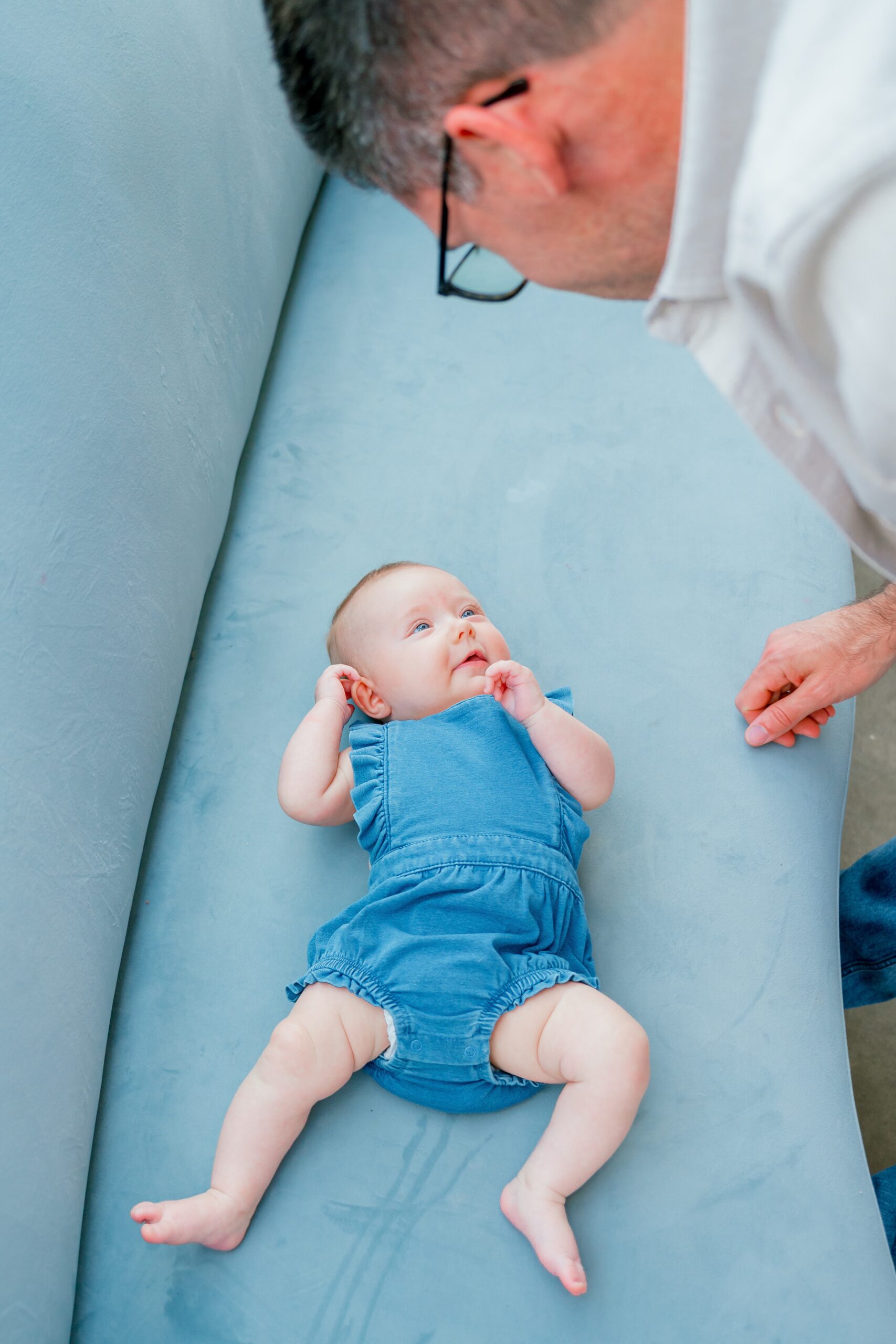 A baby girl looks up at dad while laying on a blue couch