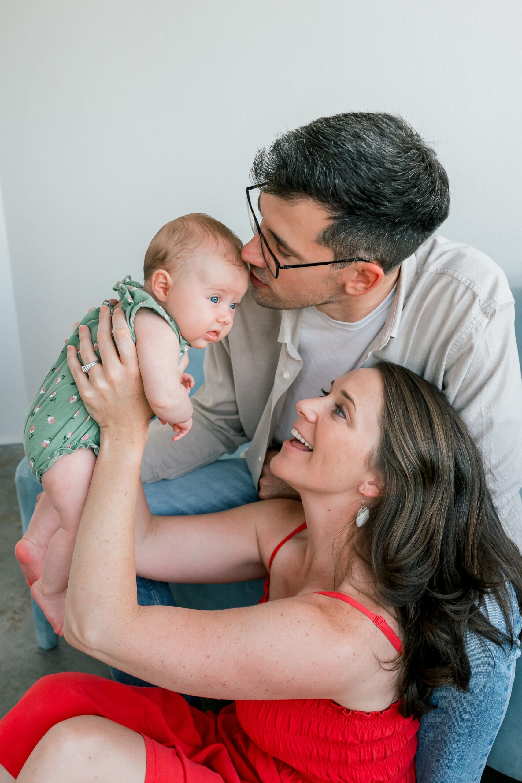 A mom and dad lift and kiss their infant in a green onesie in a photography studio in scottsdale az