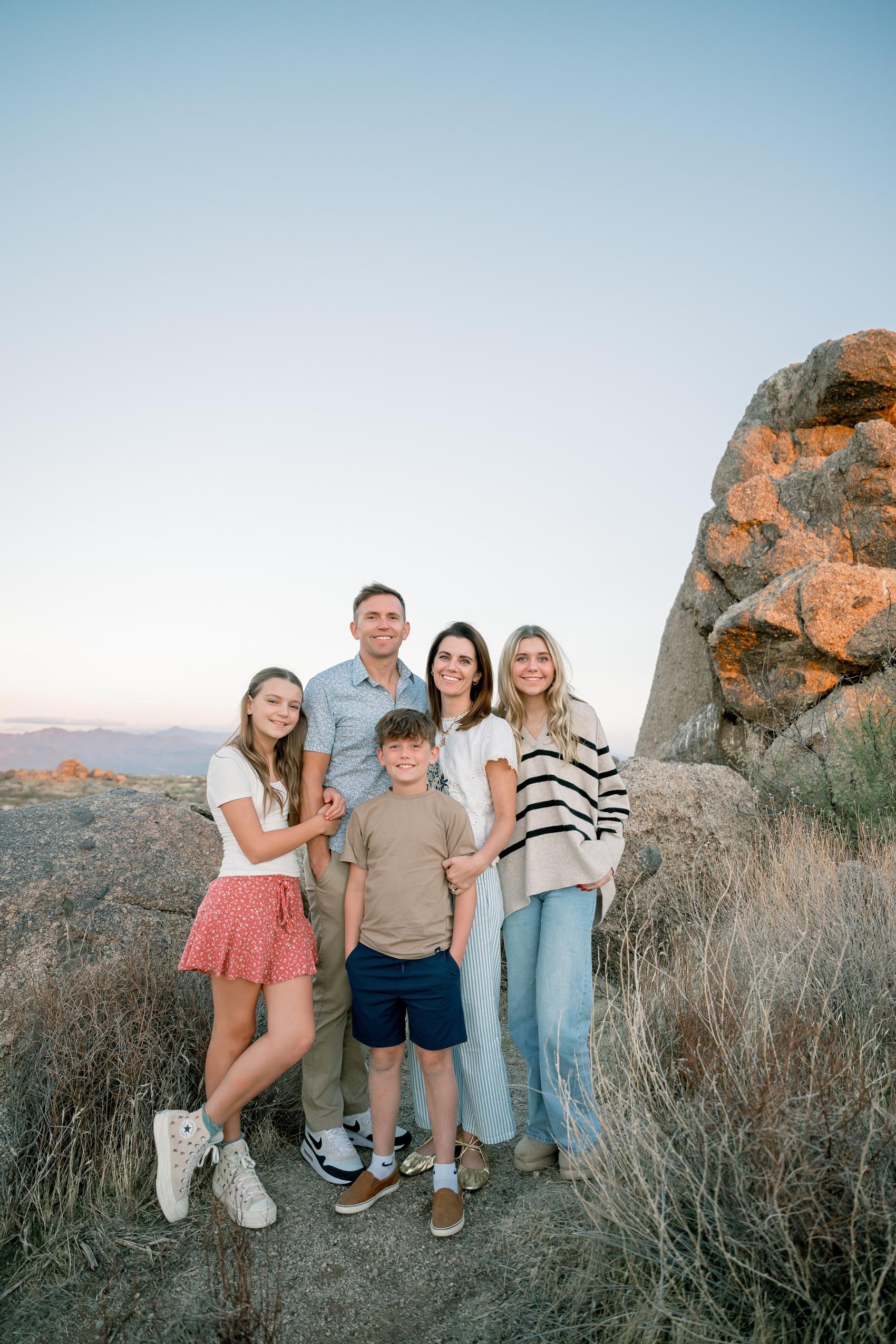 A mom and dad smile with their three children at sunset in a desert on a boulder