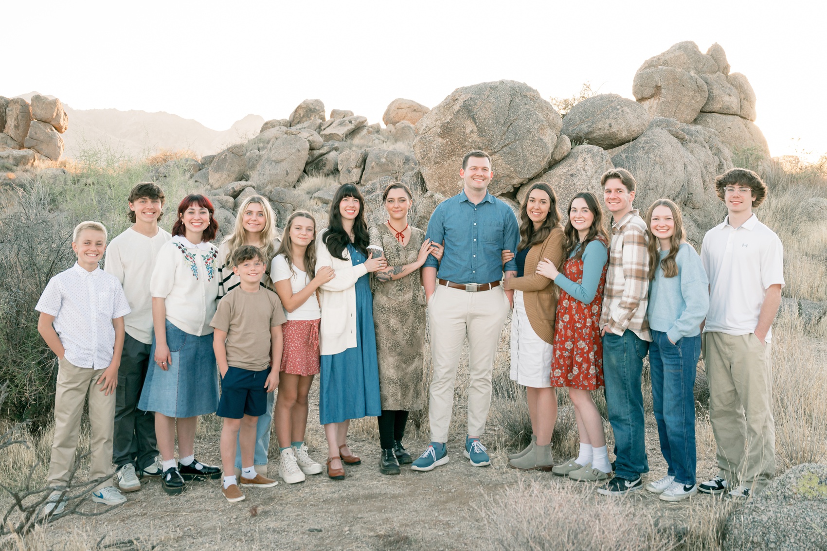 A large extended family stands smiling together and holding each other's arms in a desert trail at sunset during things to do in scottsdale with kids