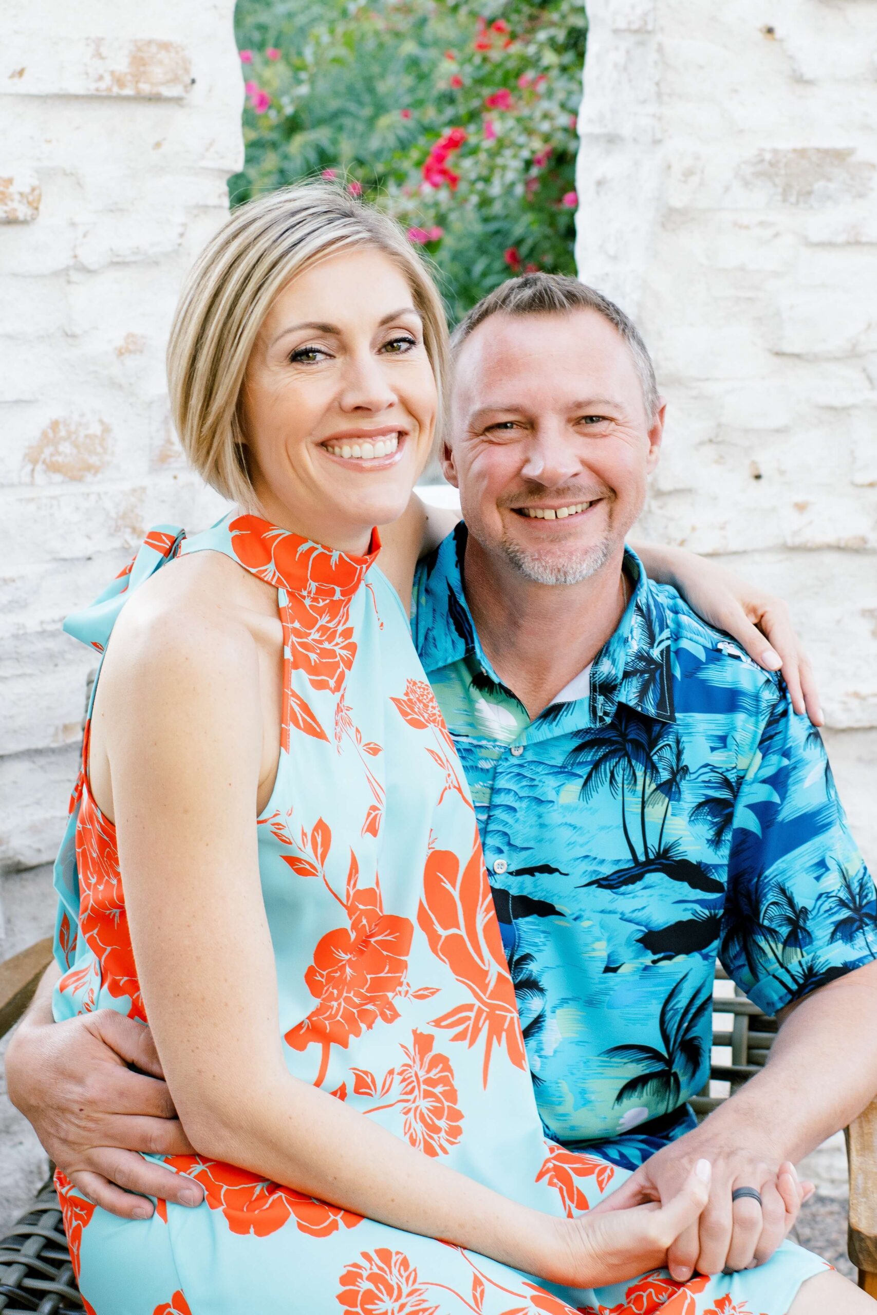 happy mom and dad in tropical outfits smile while sitting on patio furniture at one of the family friendly hotels in scottsdale