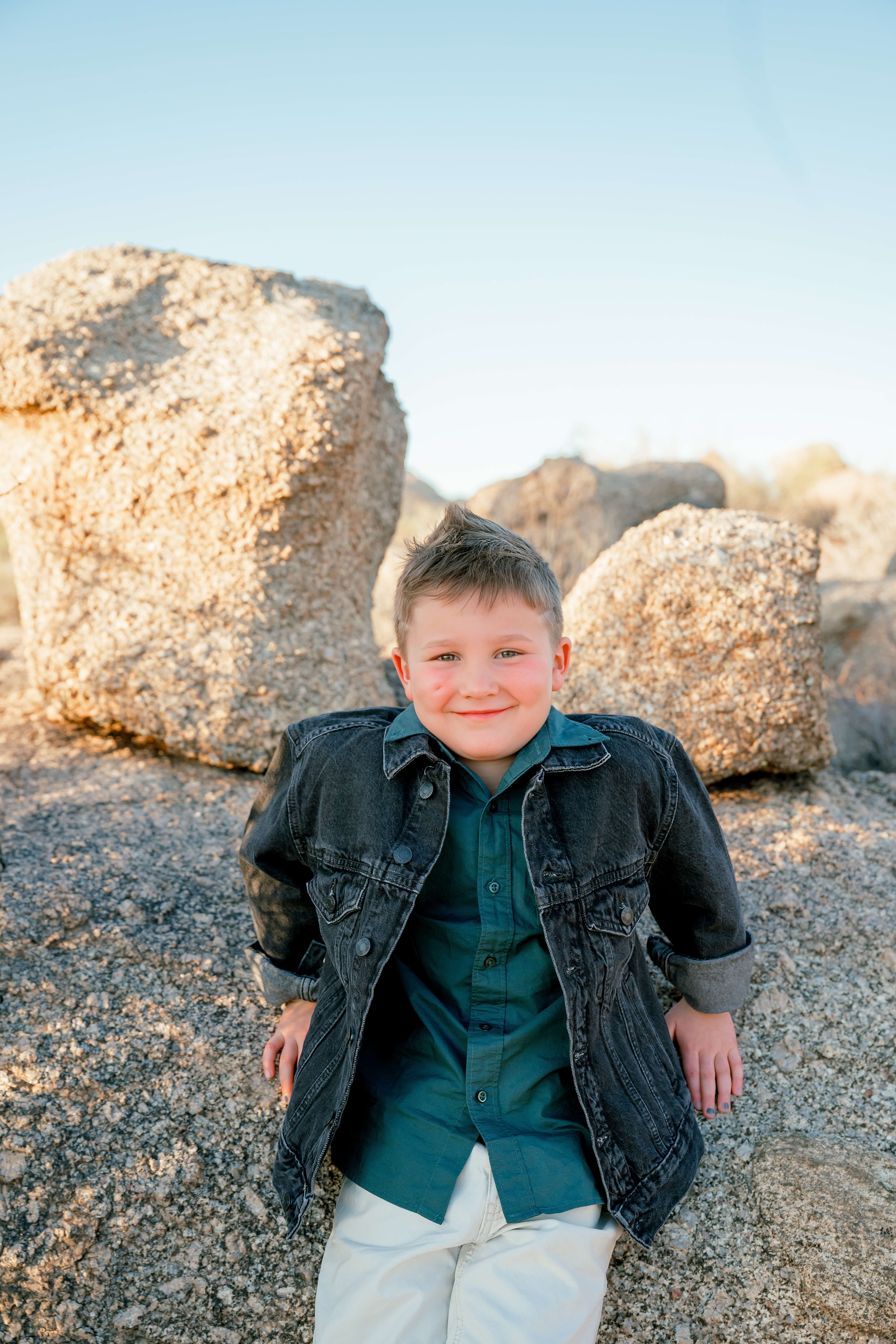 A happy young boy in a denim jacket plays on boulders at sunset before visiting indoor playgrounds in phoenix