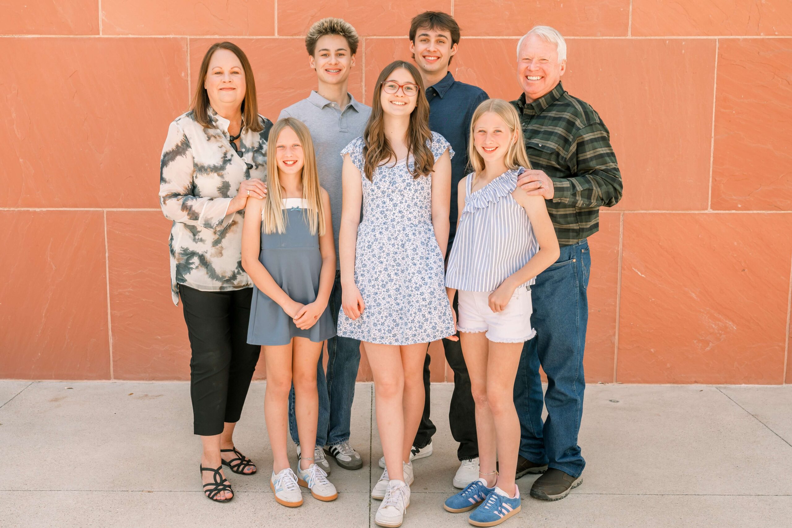 smiling mom and dad stand with their five teen children between them against an orange wall after finding kid-friendly restaurants in phoenix