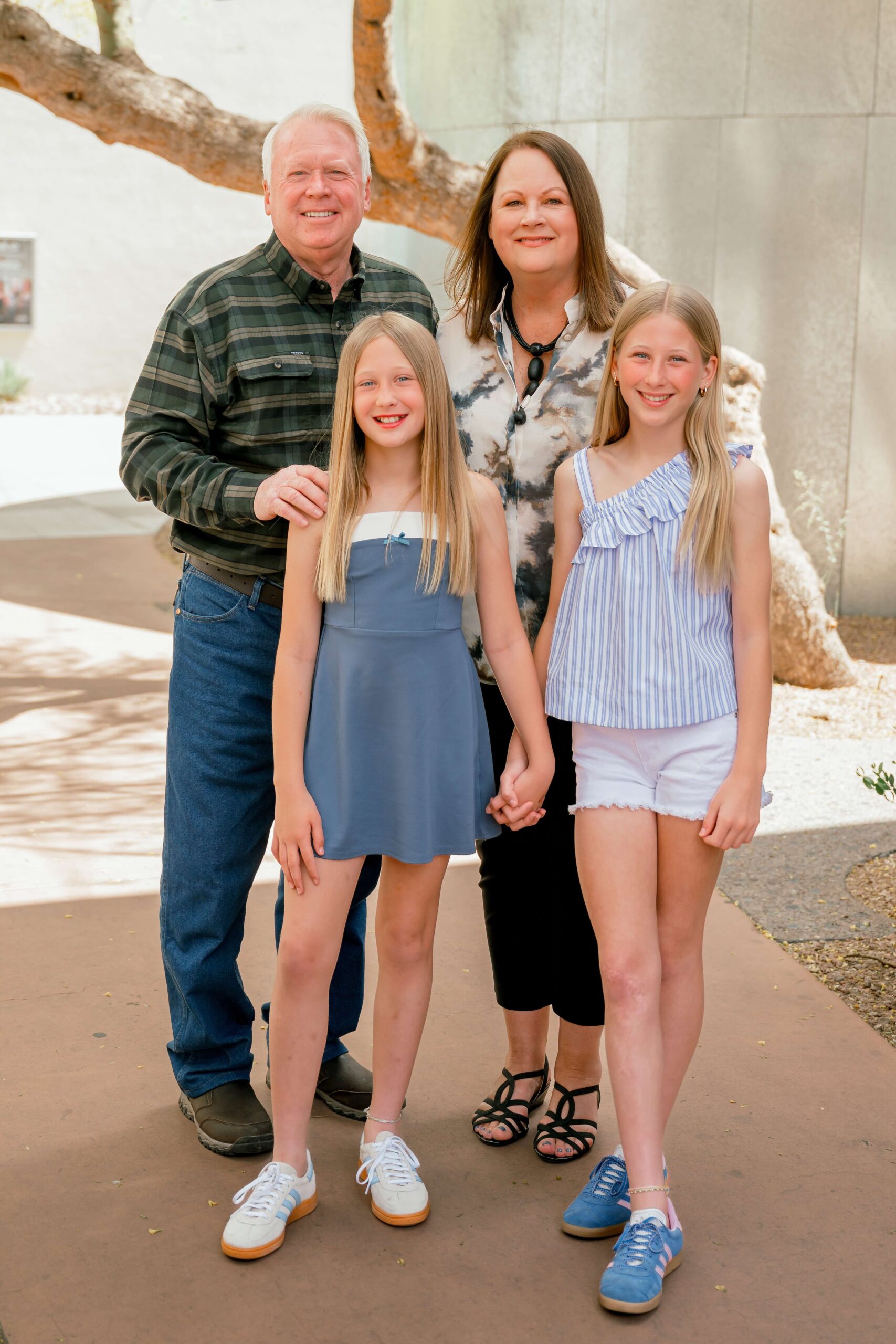 a happy mom and dad stand with their young daughters standing in front of them in blue holding hands after visiting kid-friendly restaurants in phoenix