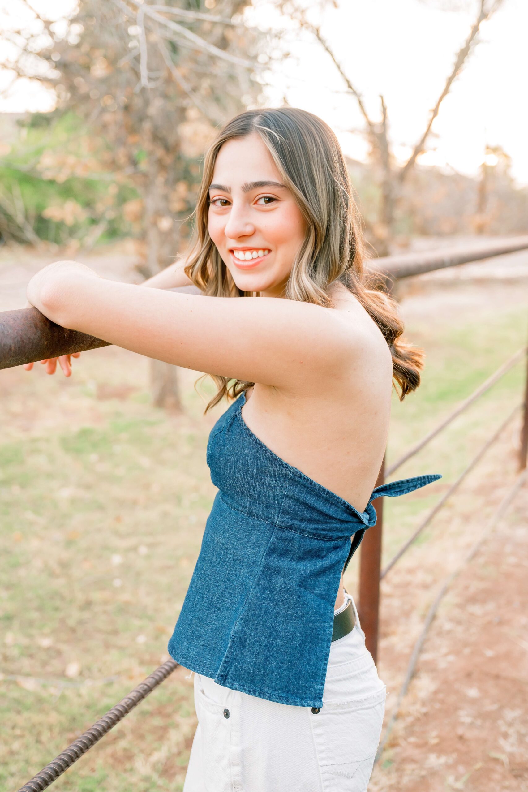 A high school senior leans on a metal railing in a park at sunset in a denim blouse after exploring boutiques in phoenix