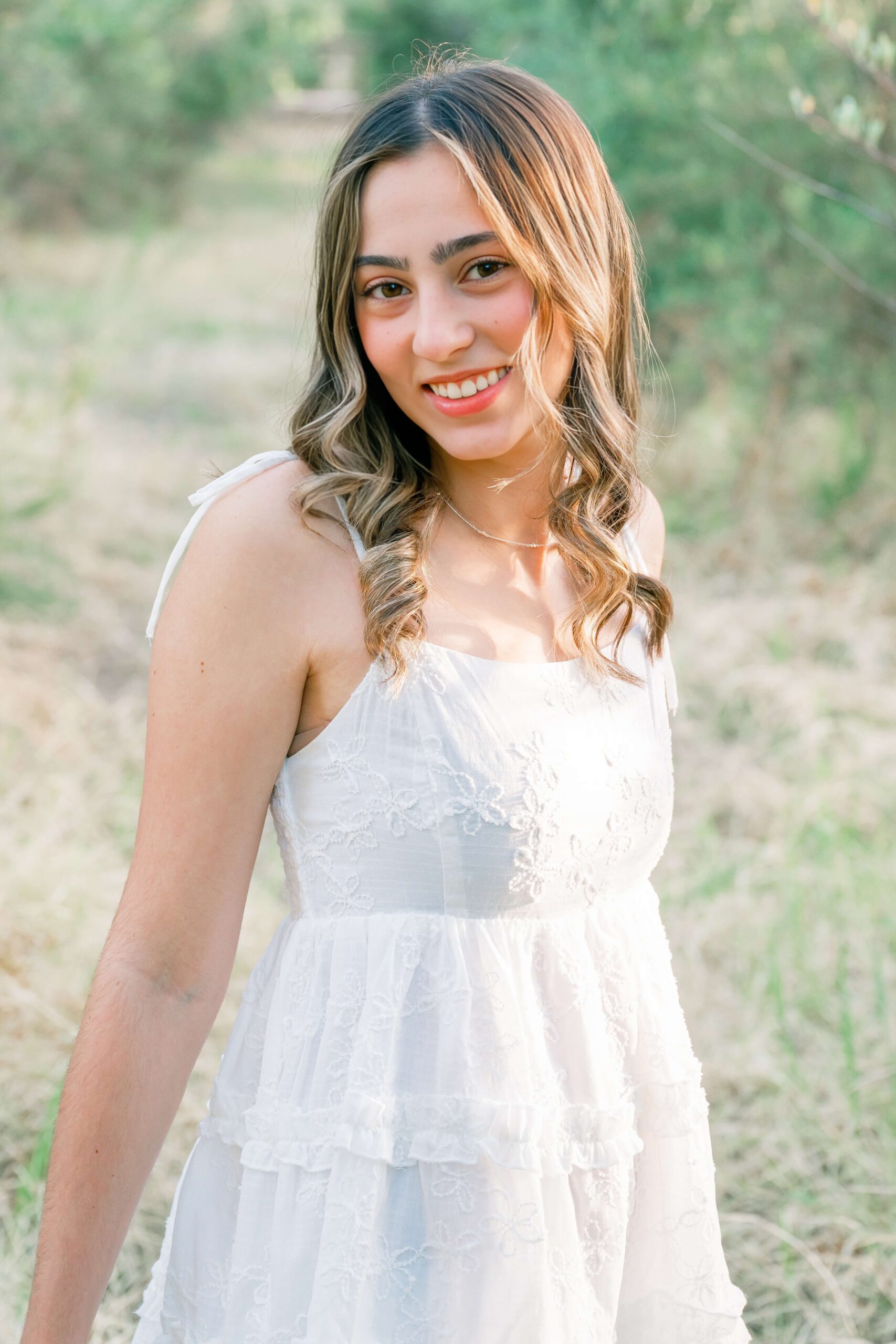 A high school senior in a white dress walks in a park at sunset after searching for prom dresses in phoenix