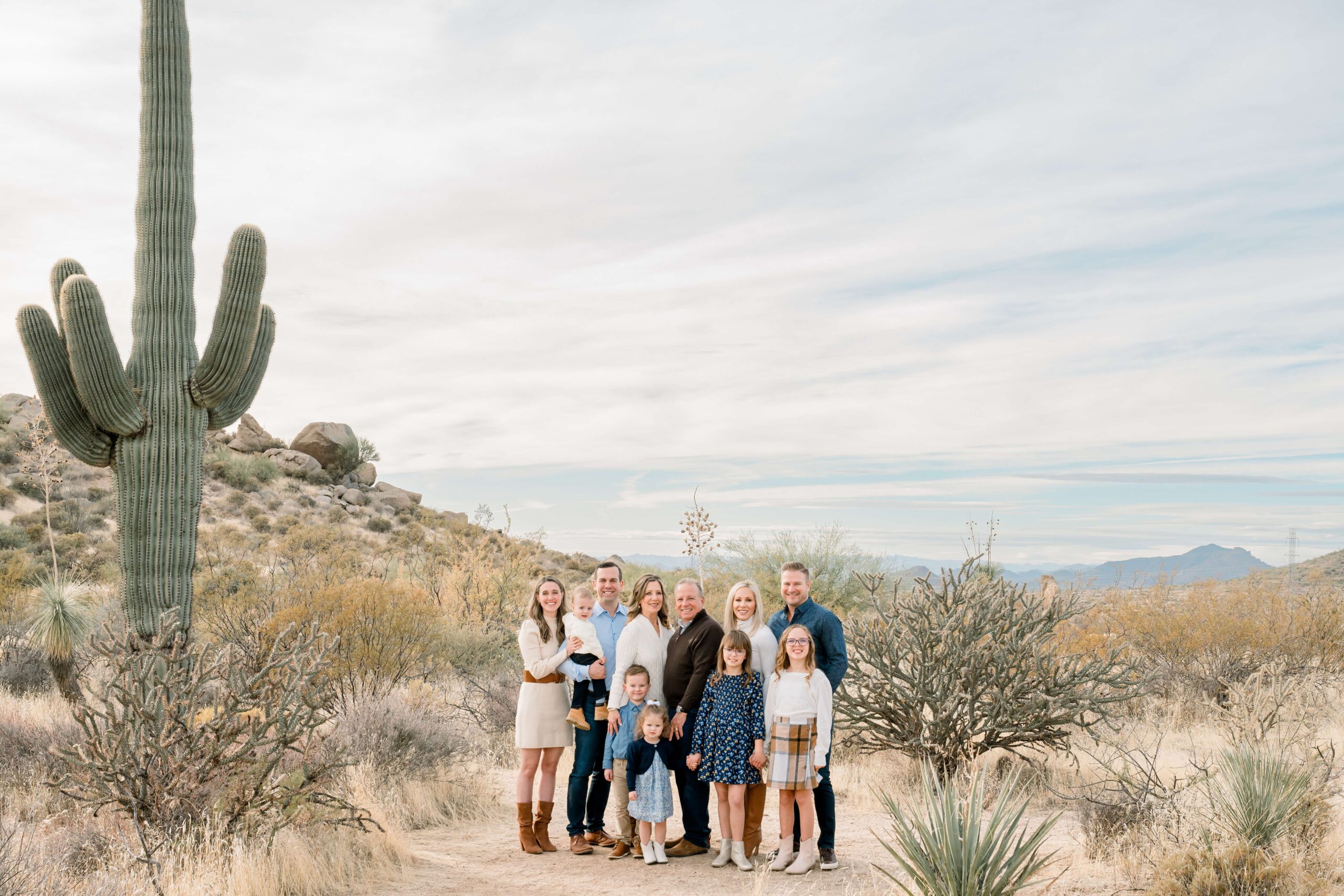 A large extended family stands in a desert trail smiling with three generations