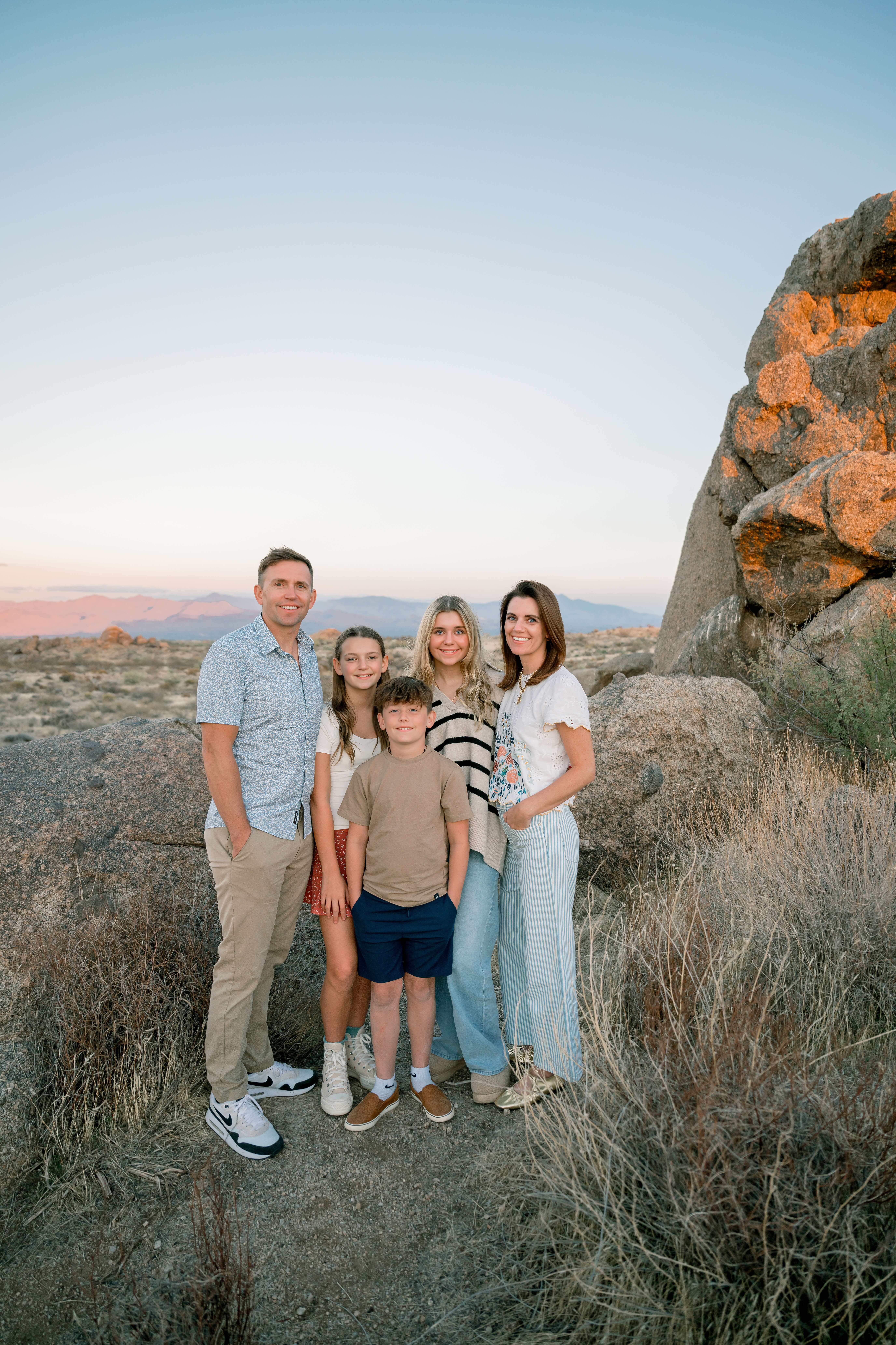 A mom and dad stand with their three children by some boulders at sunset during things to do with kids in phoenix