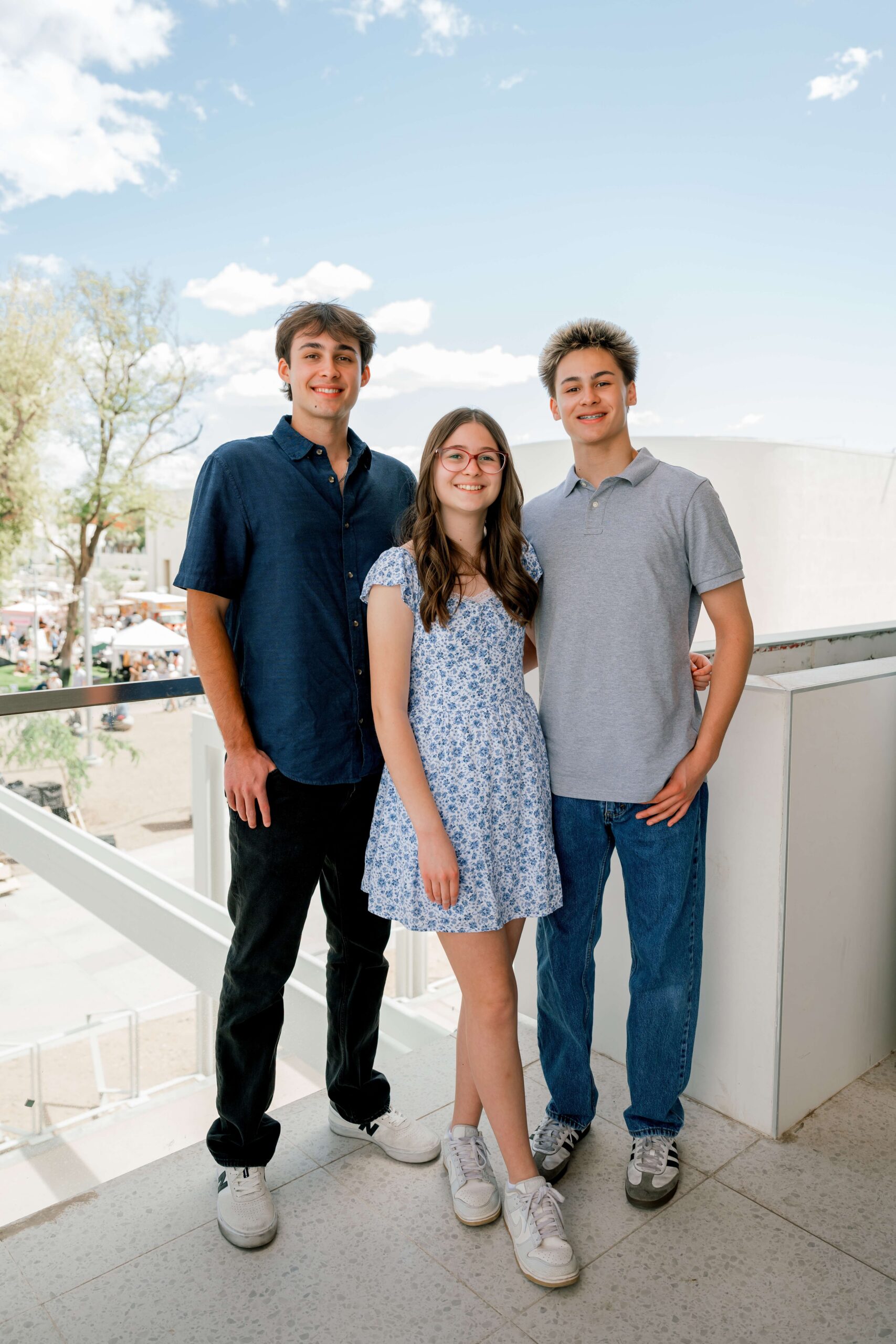 Teen brothers and sister stand on a balcony smiling together before enjoying some family things to do in phoenix at night