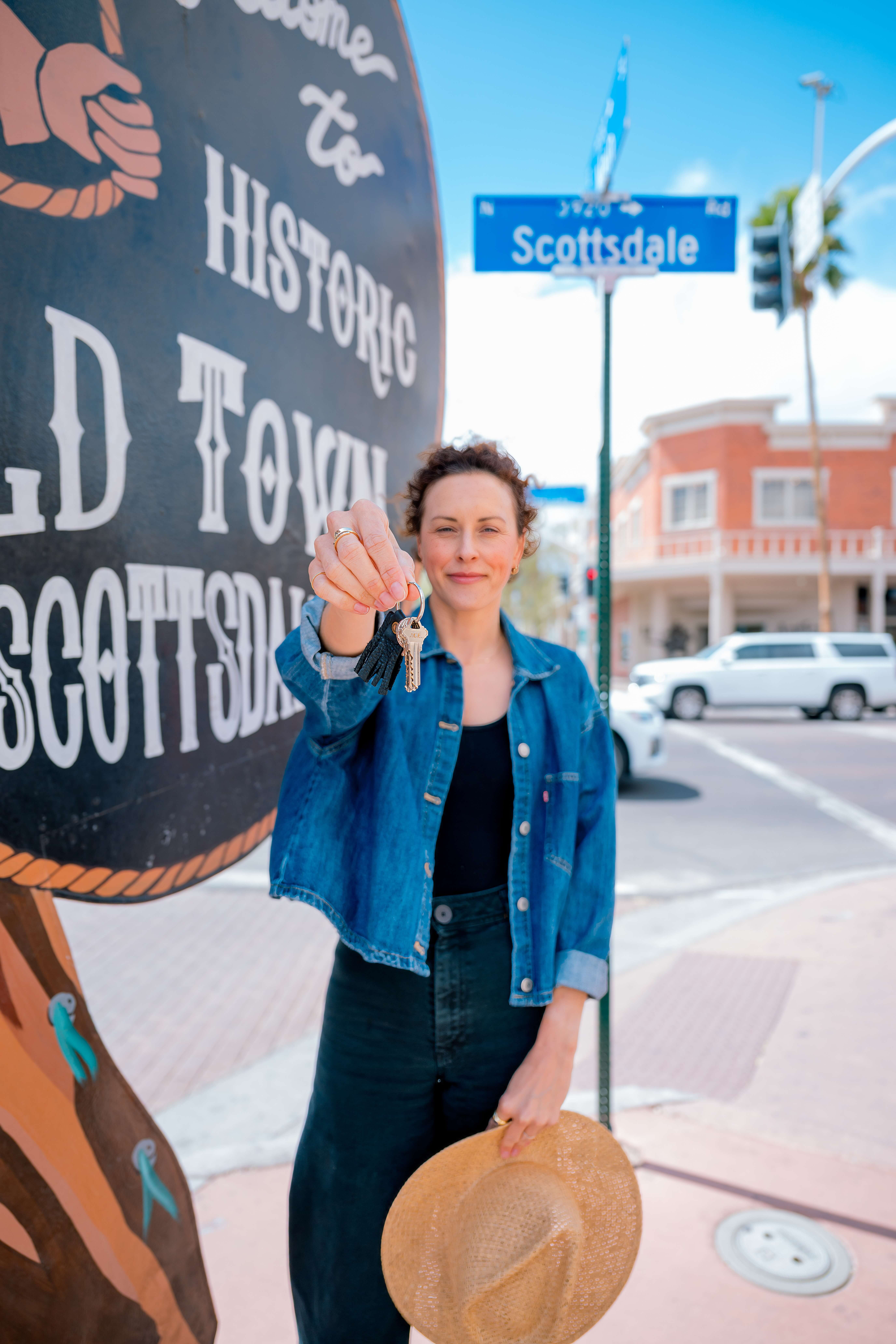 A woman holds out the keys to a store in a denim jacket in old town scottsdale for her branding photos