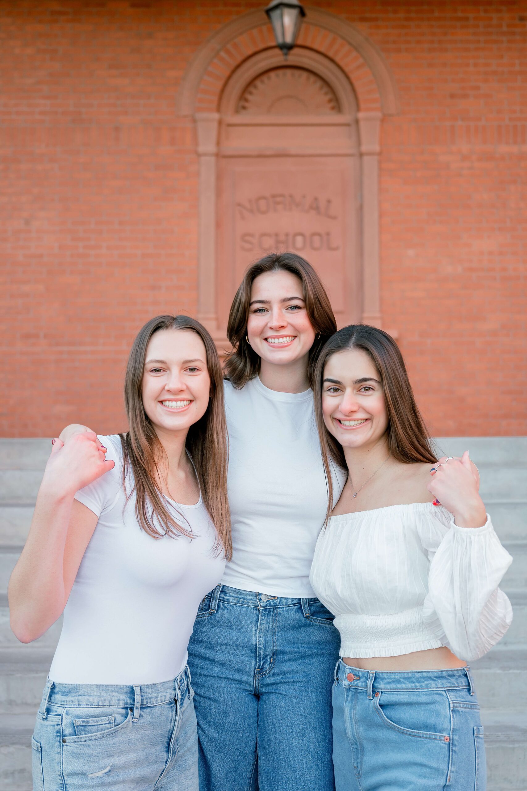 Three happy college grads stand smiling in white shirts and jeans after visiting tanning salons in phoenix with arms around each other