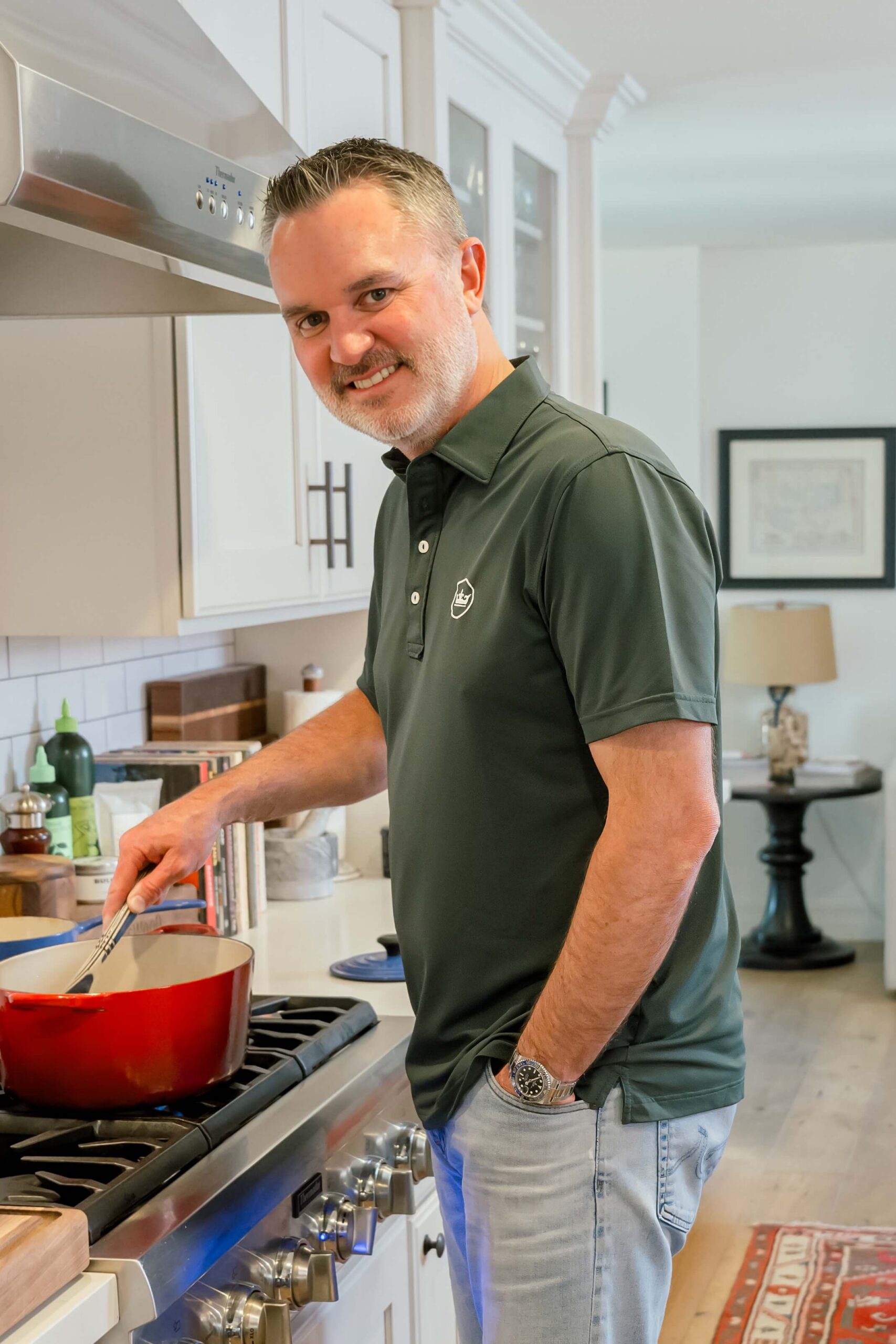A man in a green polo stirs something cooking in a pot in a kitchen after finding How to Stand Out in a Saturated Market