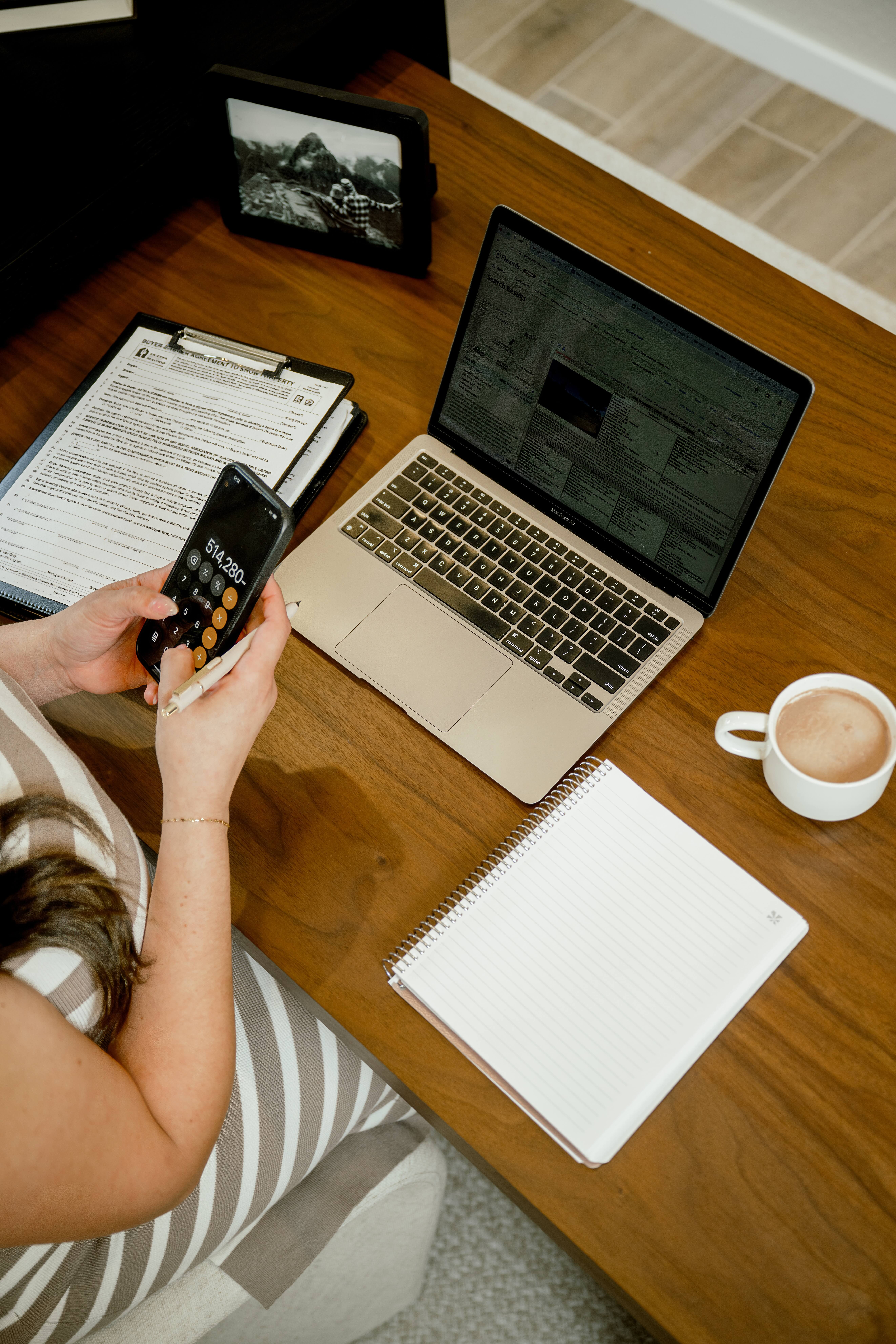 A look down at a woman typing into her phone calculator at her desk with a coffee for her must-have brand photos