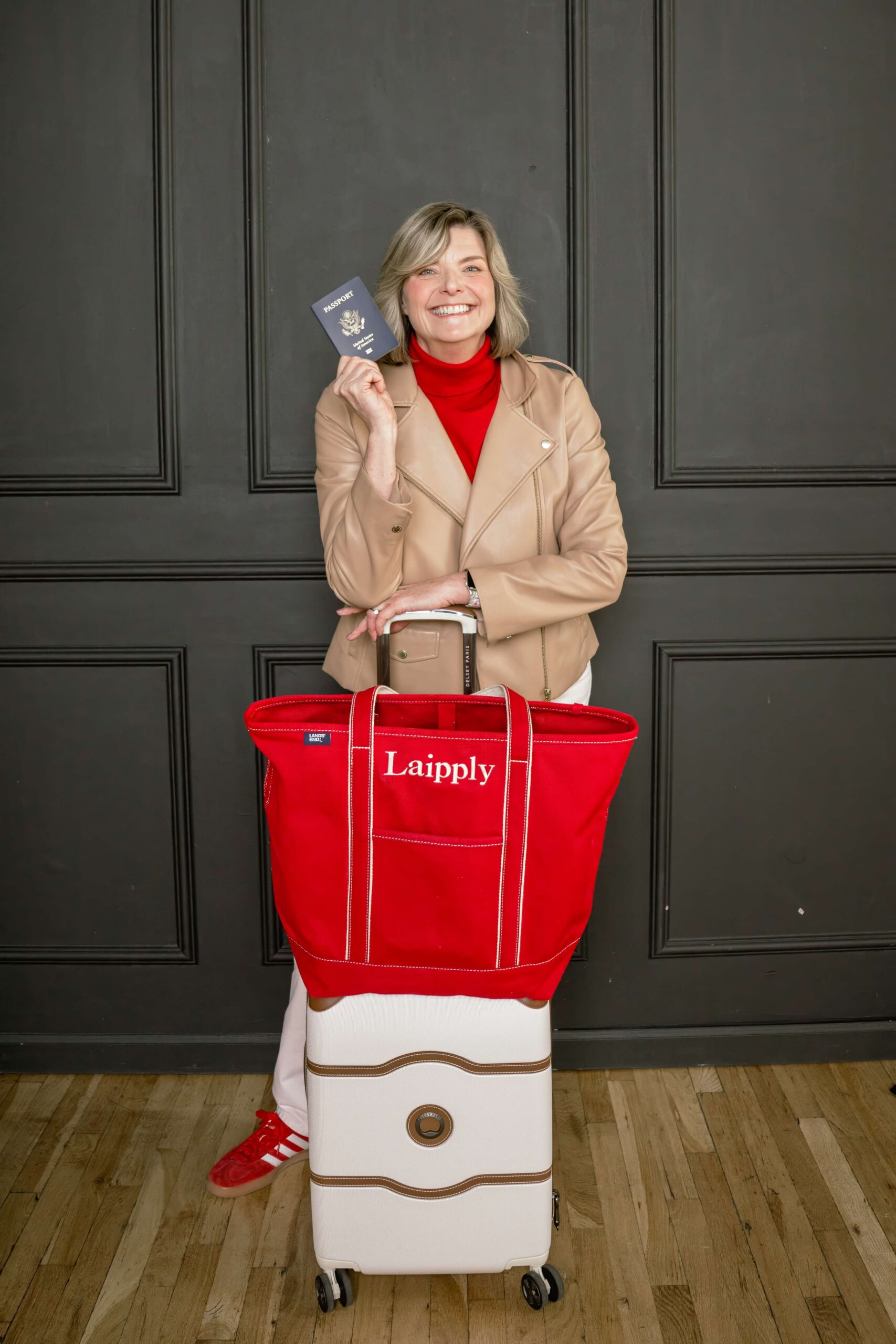 A smiling woman holds up her passport behind her luggage while posing for brand photos